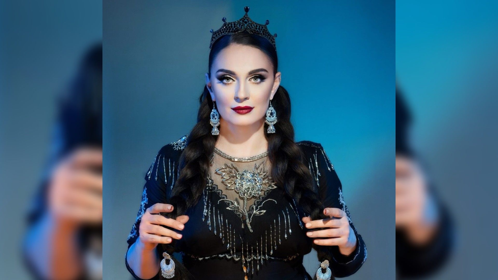Елена Ваенга в короне и вечернем платье с украшениями, стоящая на синем фоне