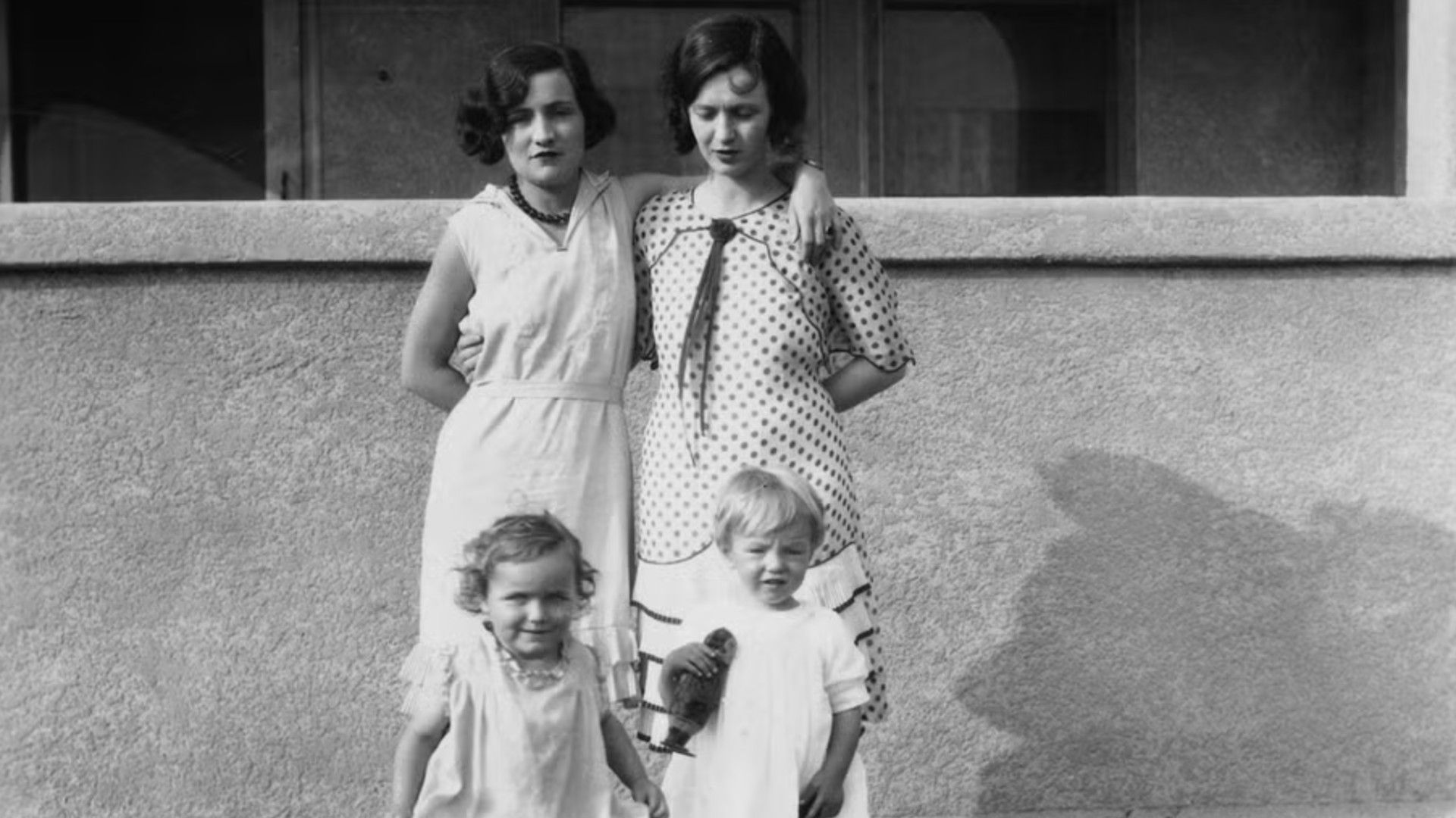 Черно-белое фото 20-х годов XX века, две женщины и две маленьких девочки стоят на фоне стены