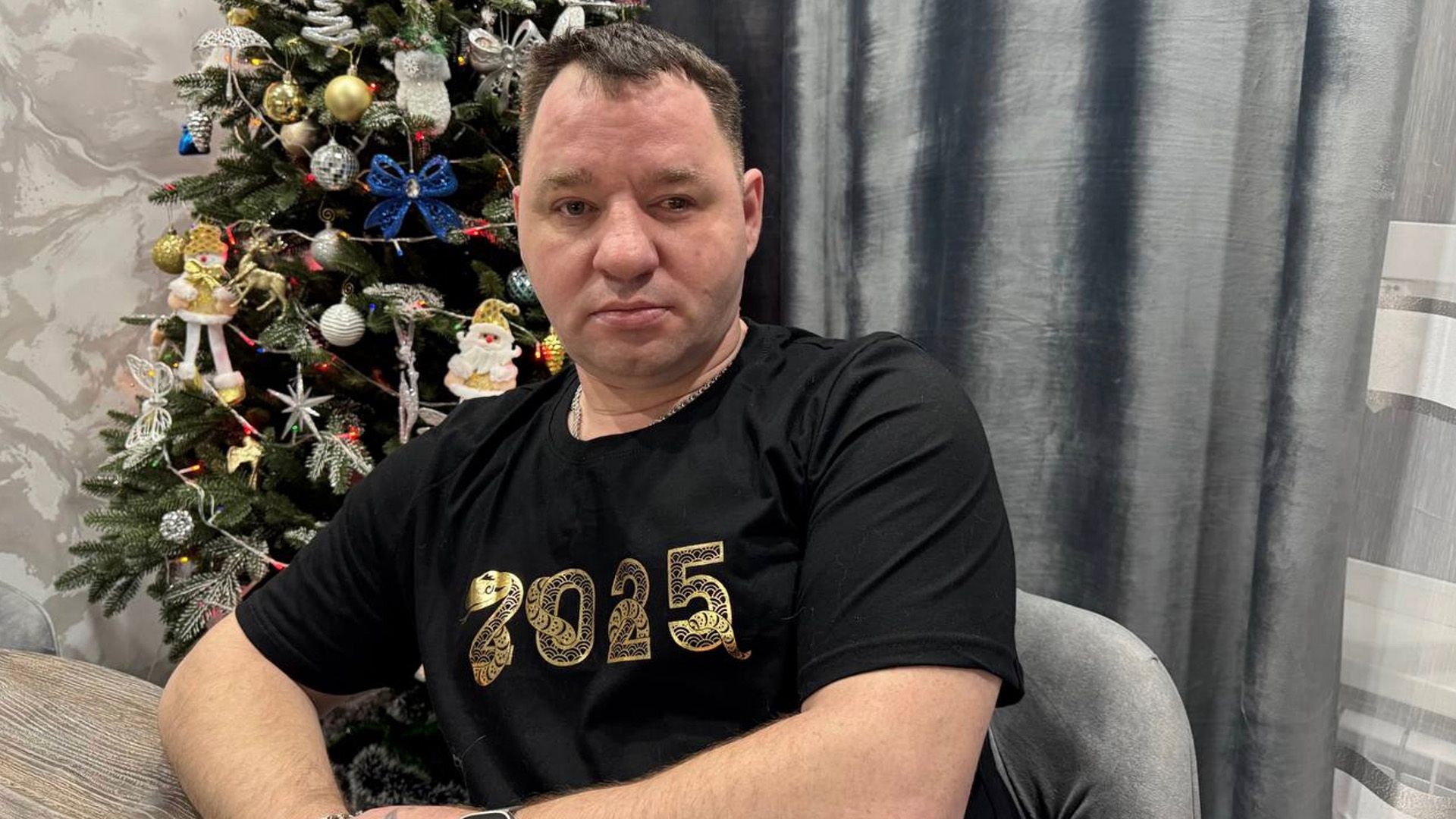 Сергей Завьялов в футболке с надписью "2025" у новогодней ёлки