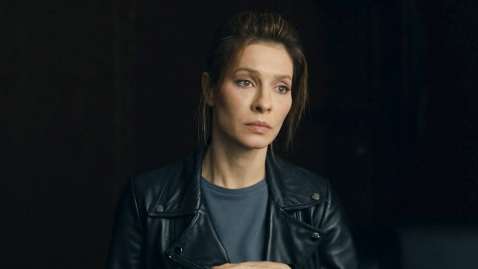 Елена Подкаминская в кожаной куртке на чёрном фоне, грустное выражение лица