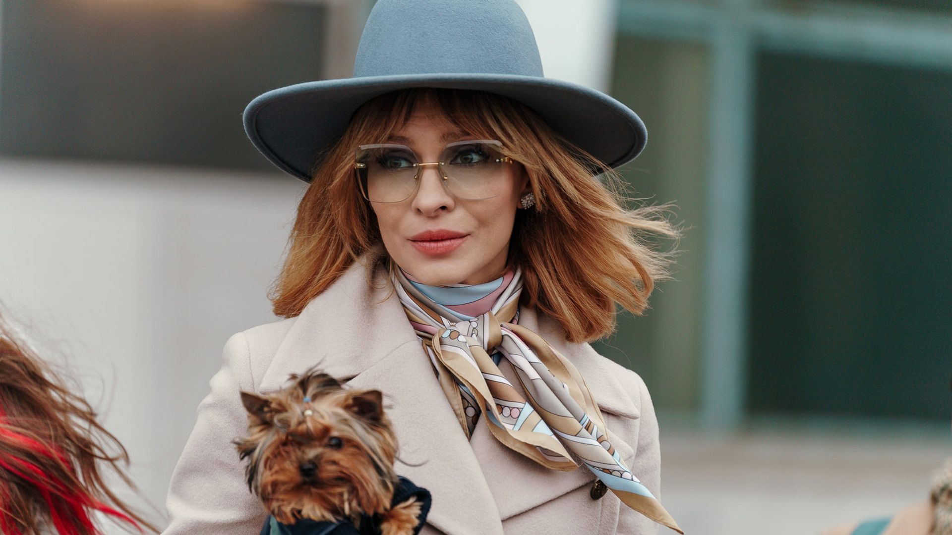 Елена Подкаминская в элегантной одежде и шляпке держит подмышкой йоркширского терьера