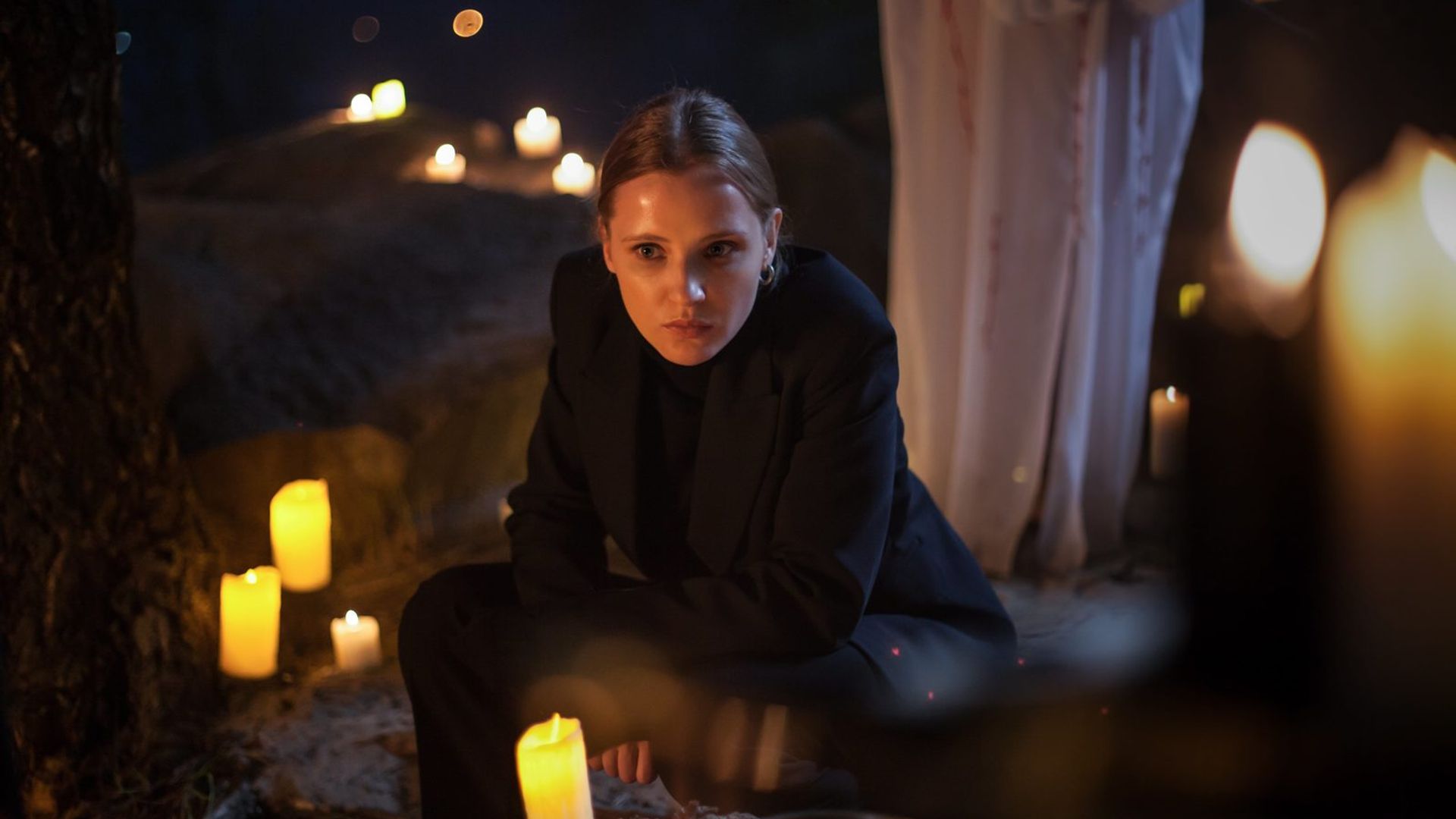 Софья Лебедева с волосами, собранными в хвост, в тёмном костюме, на переднем плане свечи