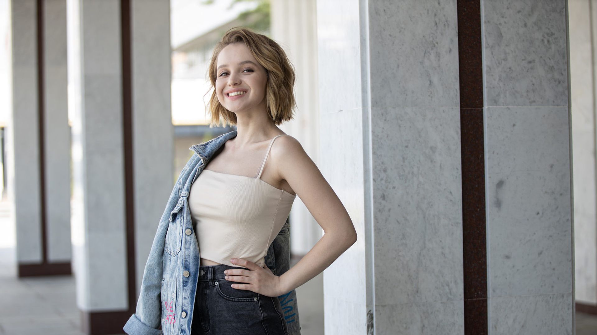 Василина Юсковец в белой футболке стоит на фоне городских зданий