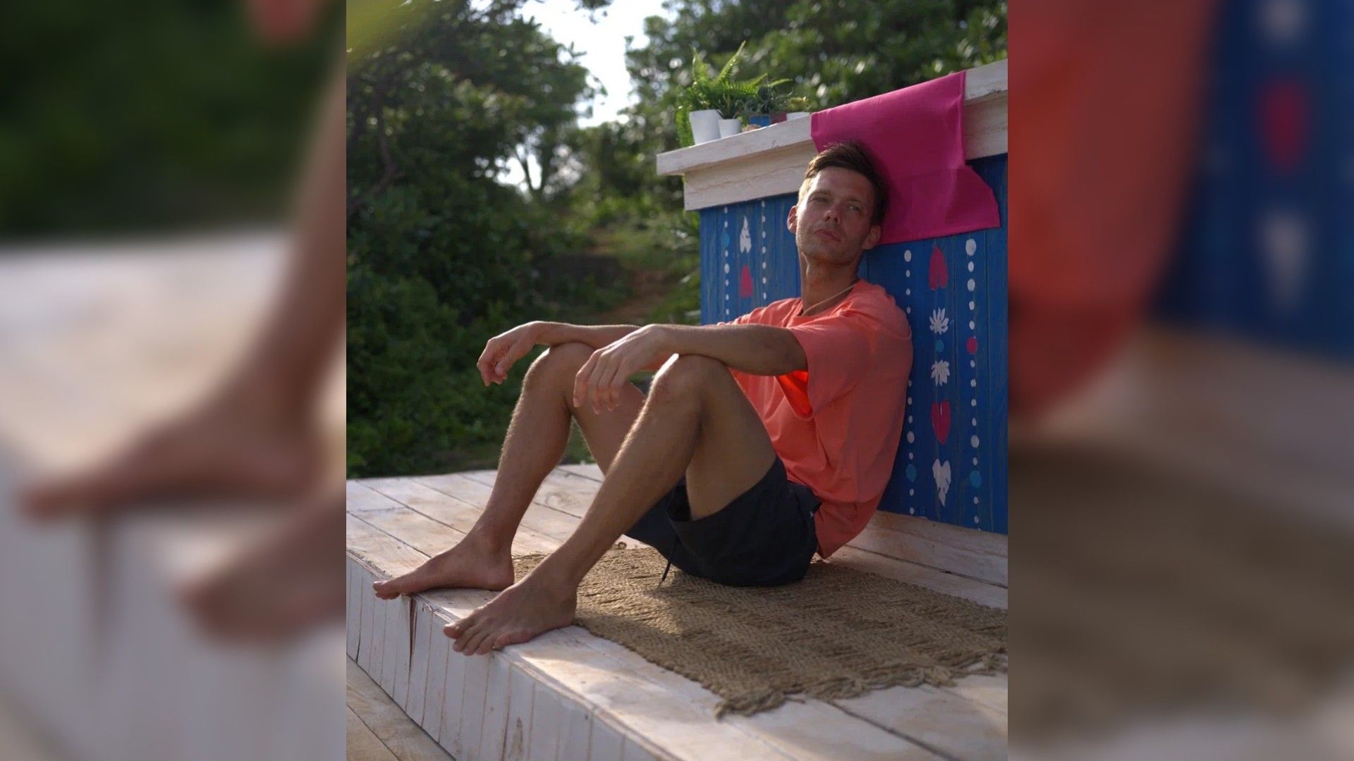 Аристарх Венес сидит, опершись спиной, в оранжевой футболке и шортах