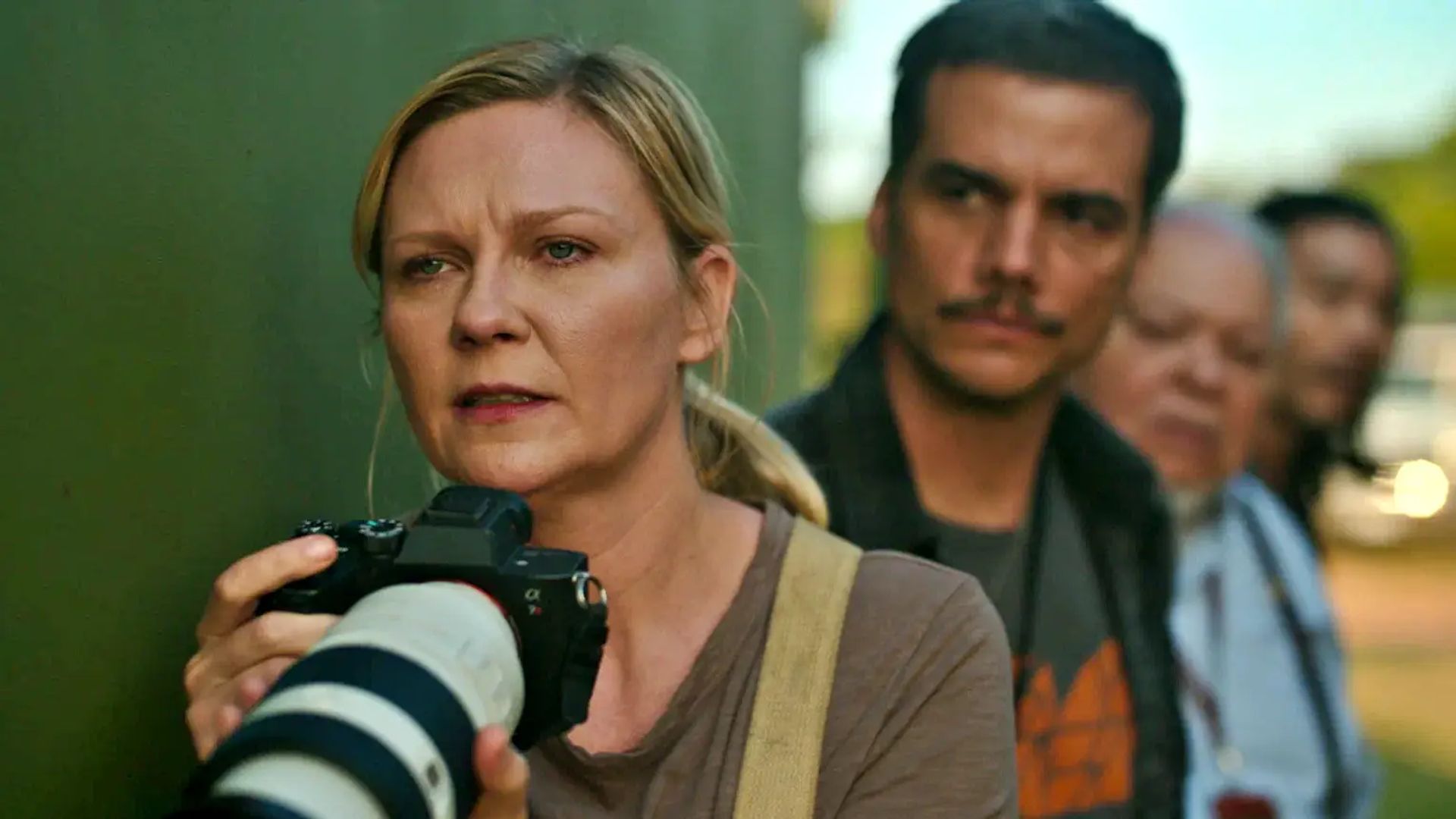 Кирстен Данст держит в руках фотоаппарат и смотрит вперред с напряжением