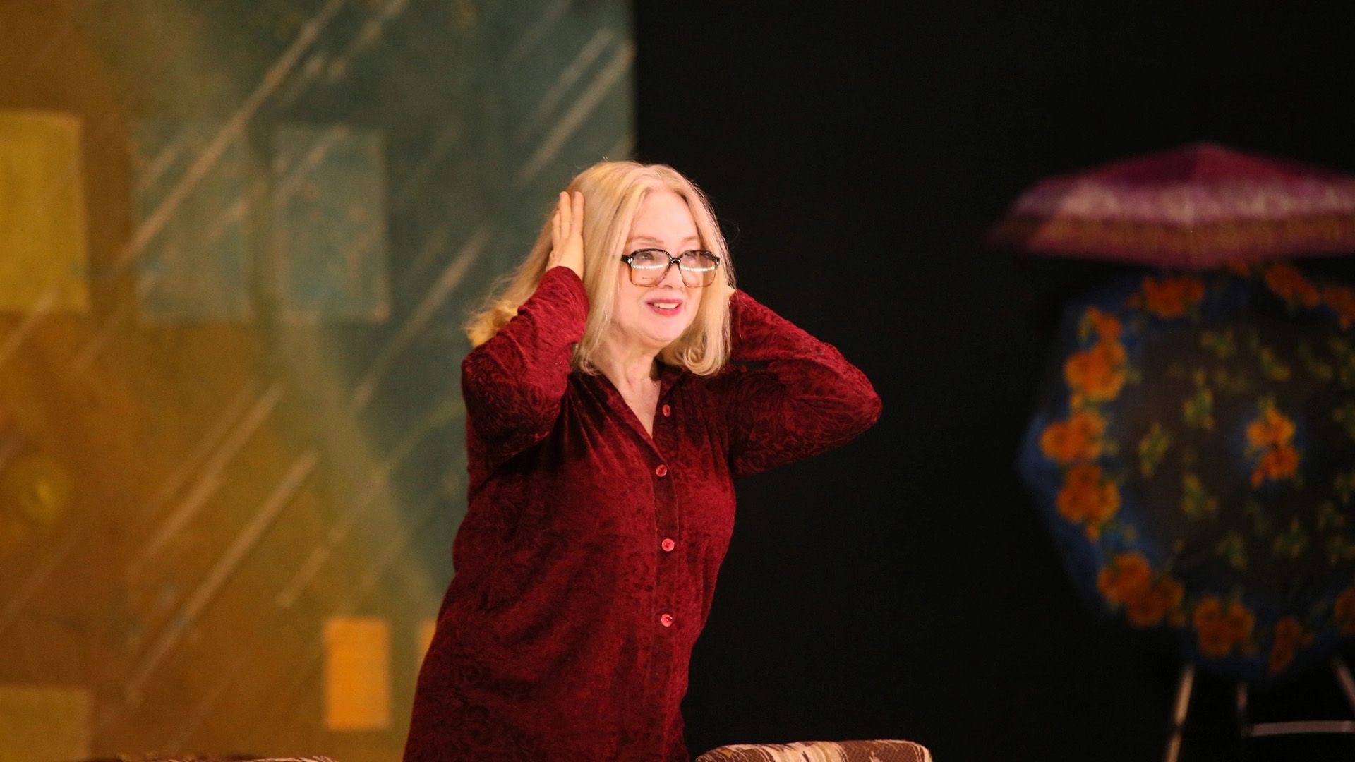 Марина Яковлева в красной бархатной блузке и больших очках держится руками за голову