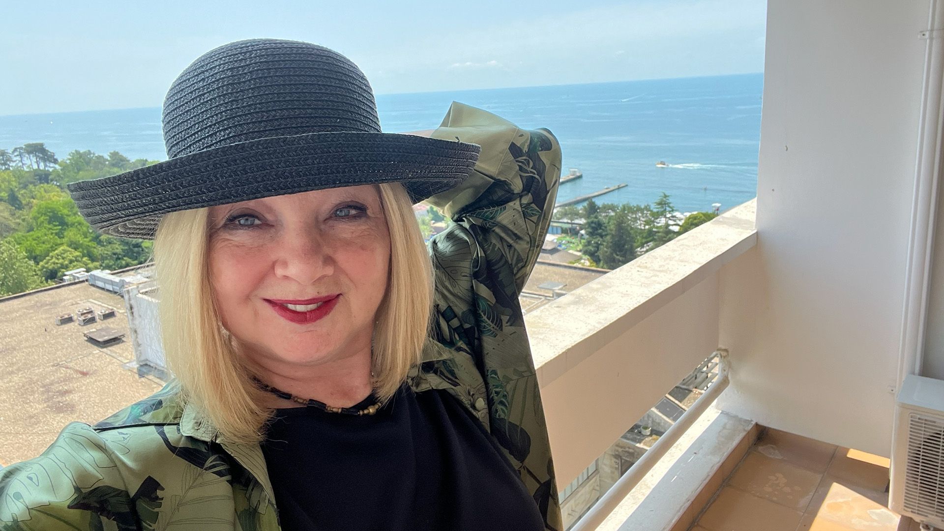 Марина Яковлева в плетеной шляпе стоит на балконе на фоне моря