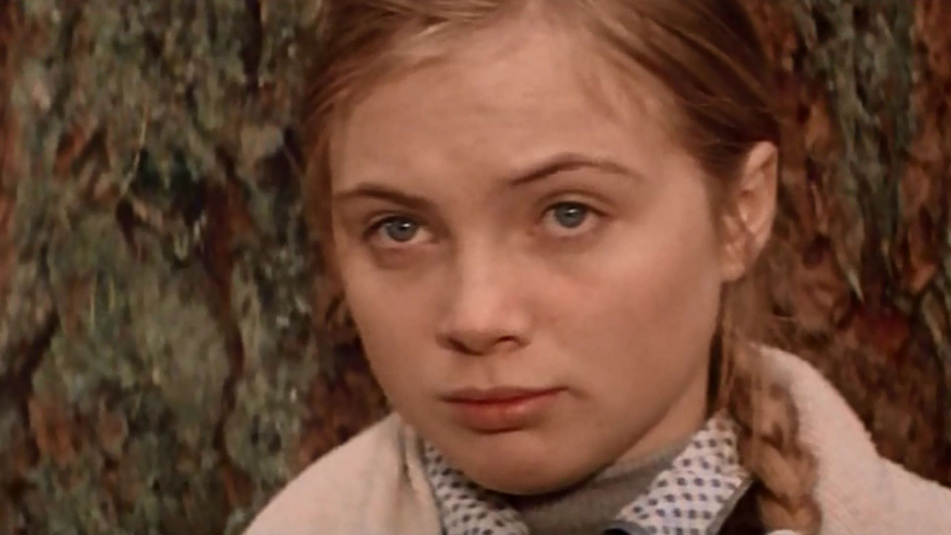 Марина Яковлева с волосами, заплетеными в косу, с грустным лицом стоит у дерева