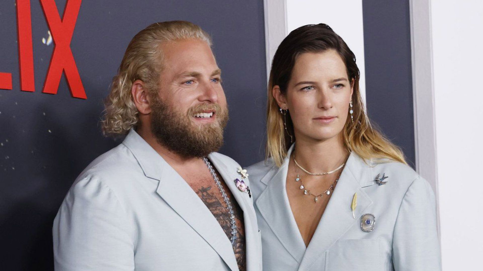 Джона Хилл и Сара Брэди позируют на фоне стены с надписью Netflix