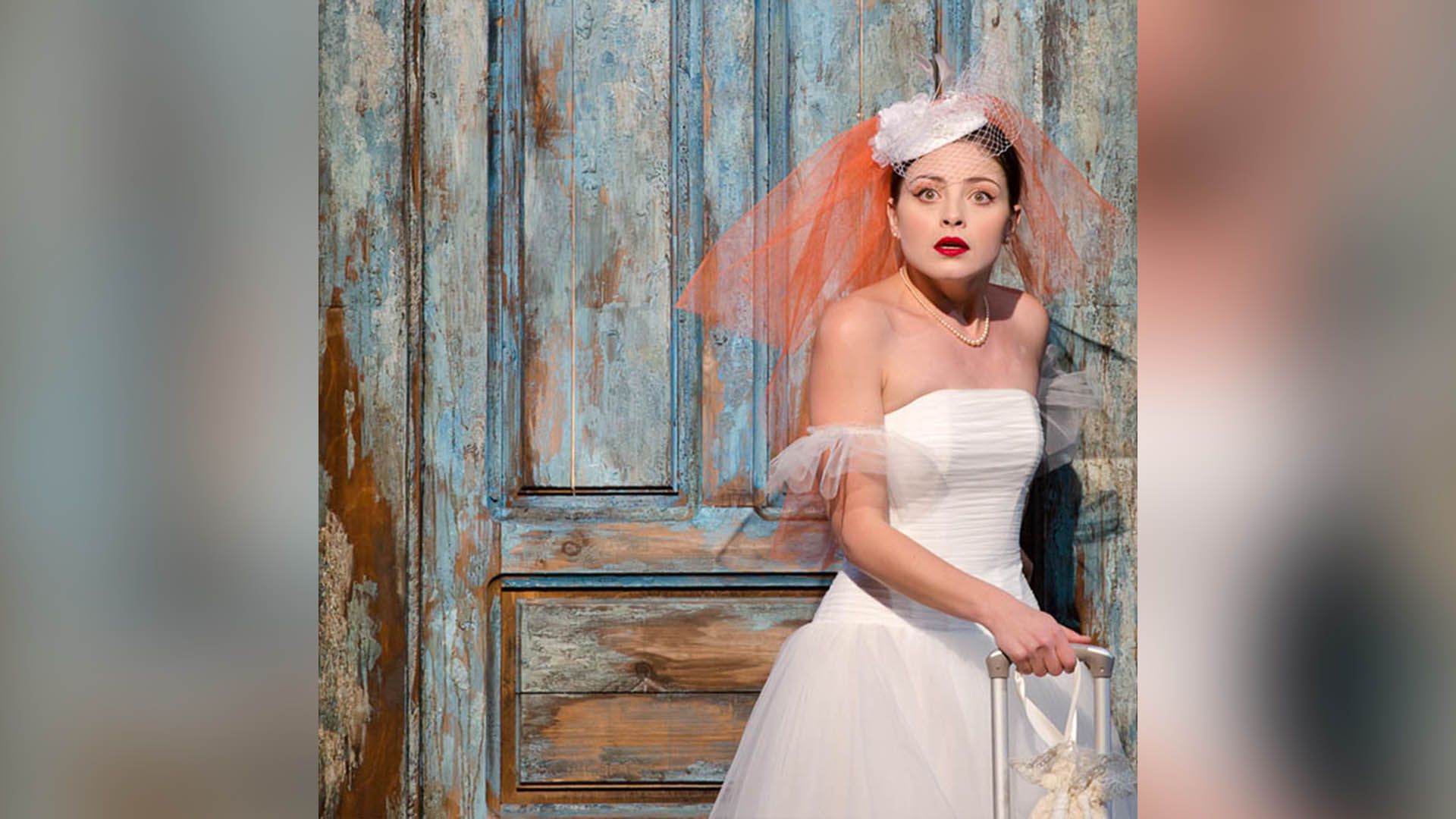 Испуганная Анастасия Тюнина в свадебном платье стоит на фоне голубой двери
