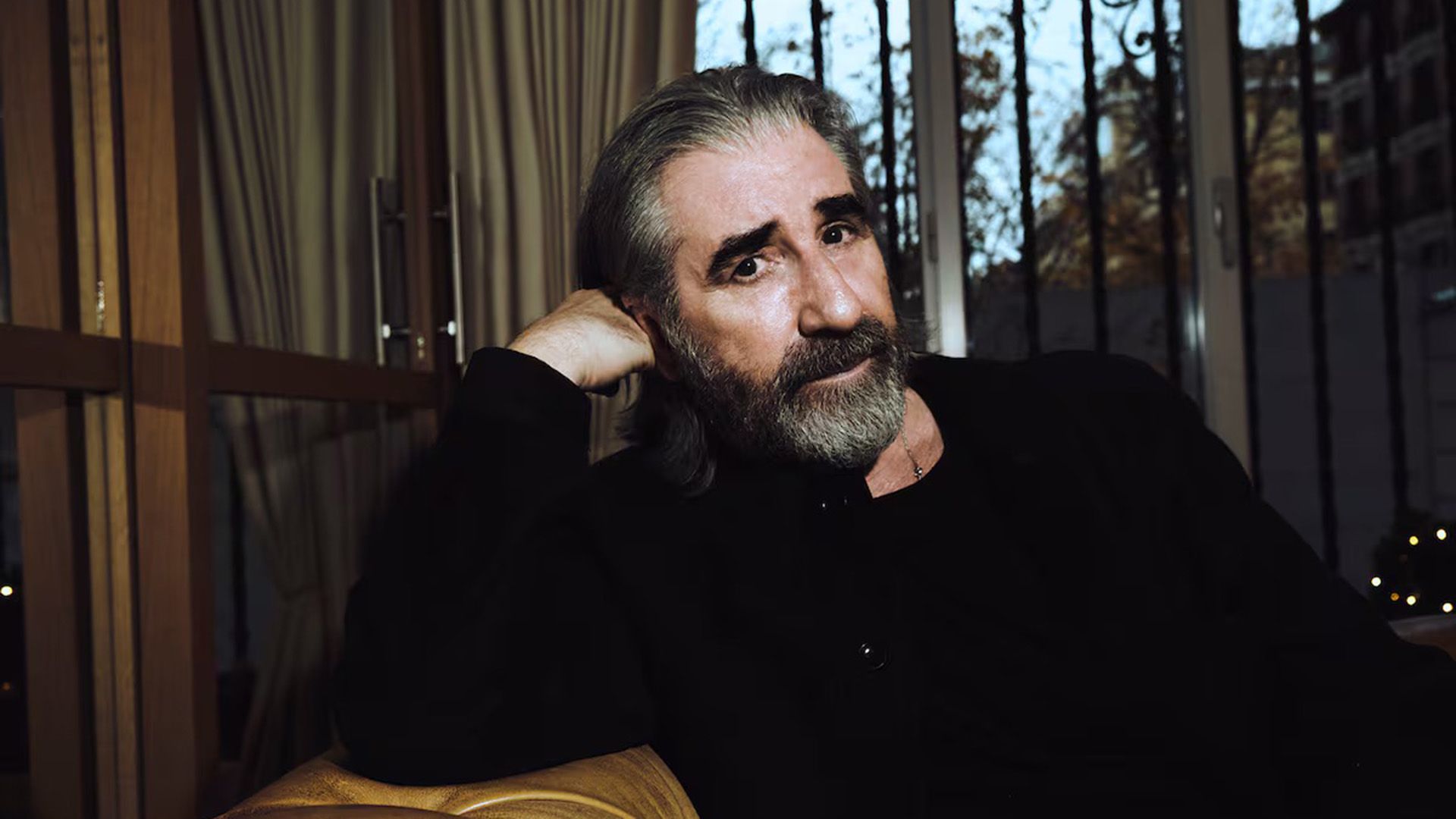 Актёр Джон Линч сидит на диване, подперев голову рукой