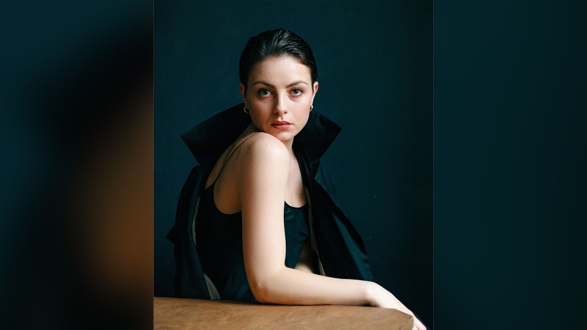 Актриса Анастасия Тюнина с золотыми серёжками в ушах сидит боком за столом