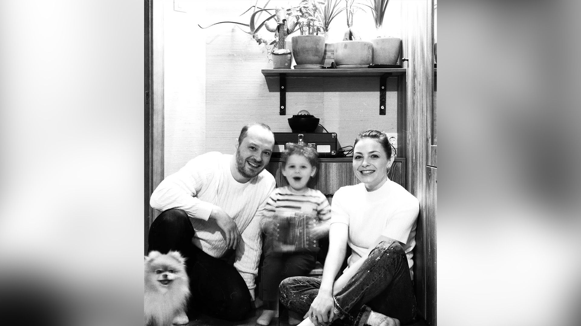 Анастасия Тюнина и Андрей Зарубин сидят на полу и смеются, между ними на стульчике сидит сын Анастасии