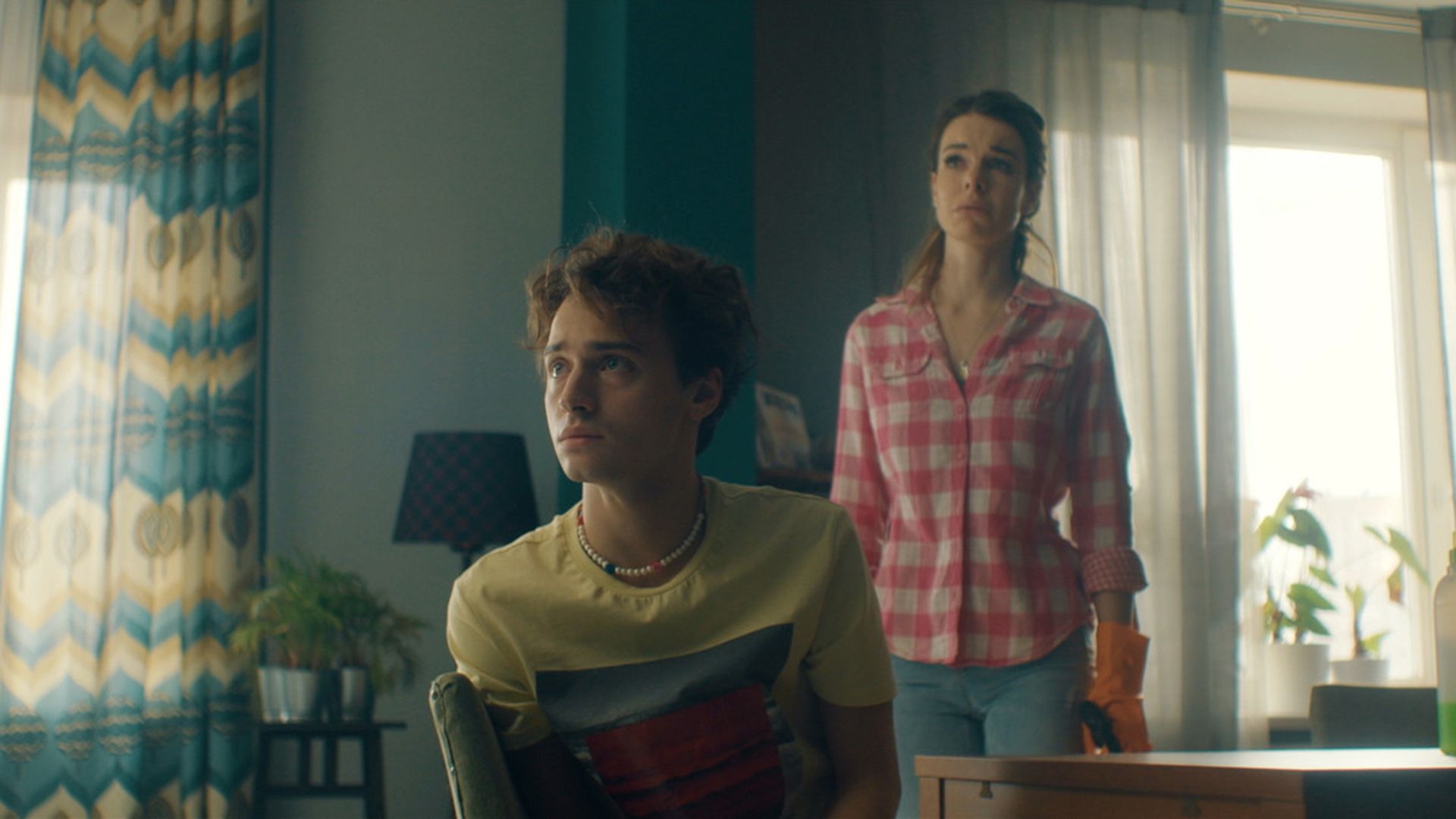 Андрей Мартынов в желтой футболке сидит на стуле, сзади стоит женщина с обеспокоенным лицом