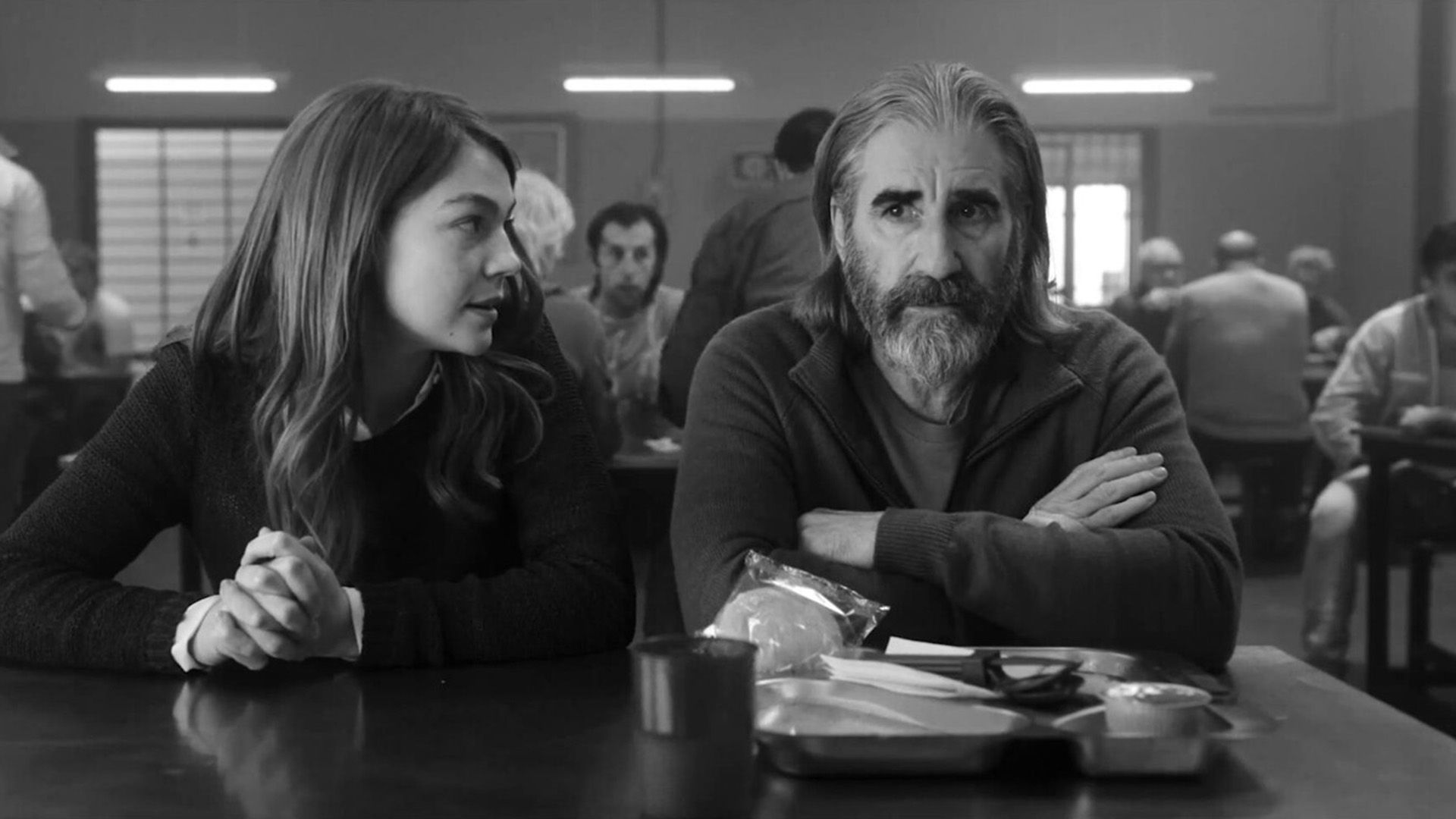 Джон Линч сидит за столом в столовой, рядом сидит девушка и что-то ему говорит