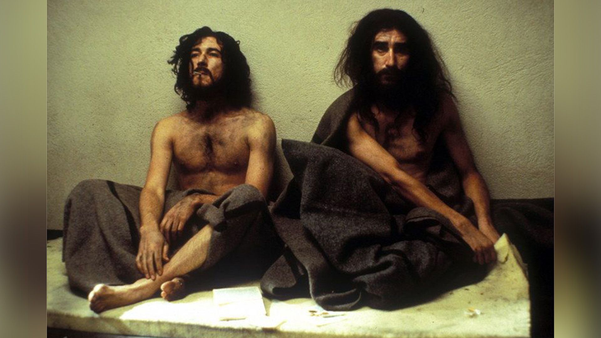 Джон Линч сидит на полу рядом с Эйданом Гилленом, оба худые и с длинными растрепанными волосами