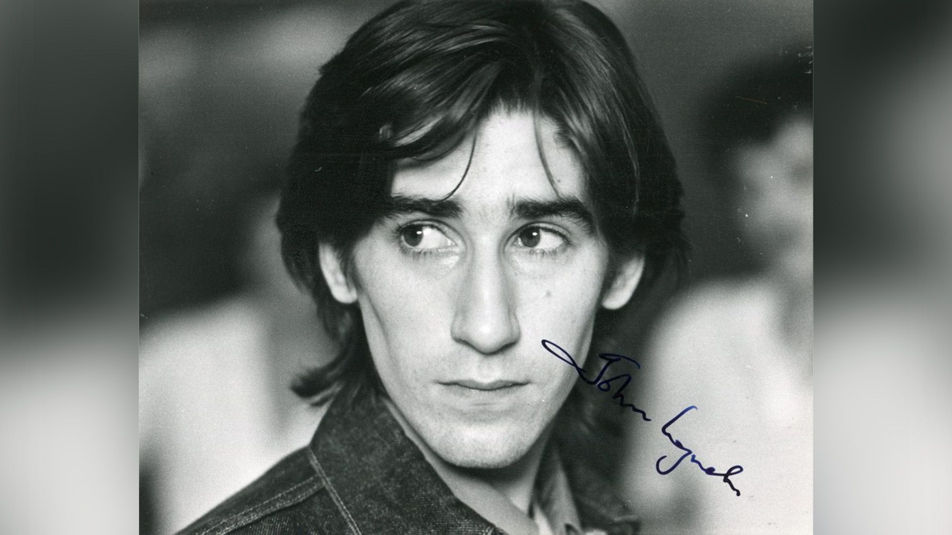 Молодой Джон Линч с длинными волосами смотрит в сторону