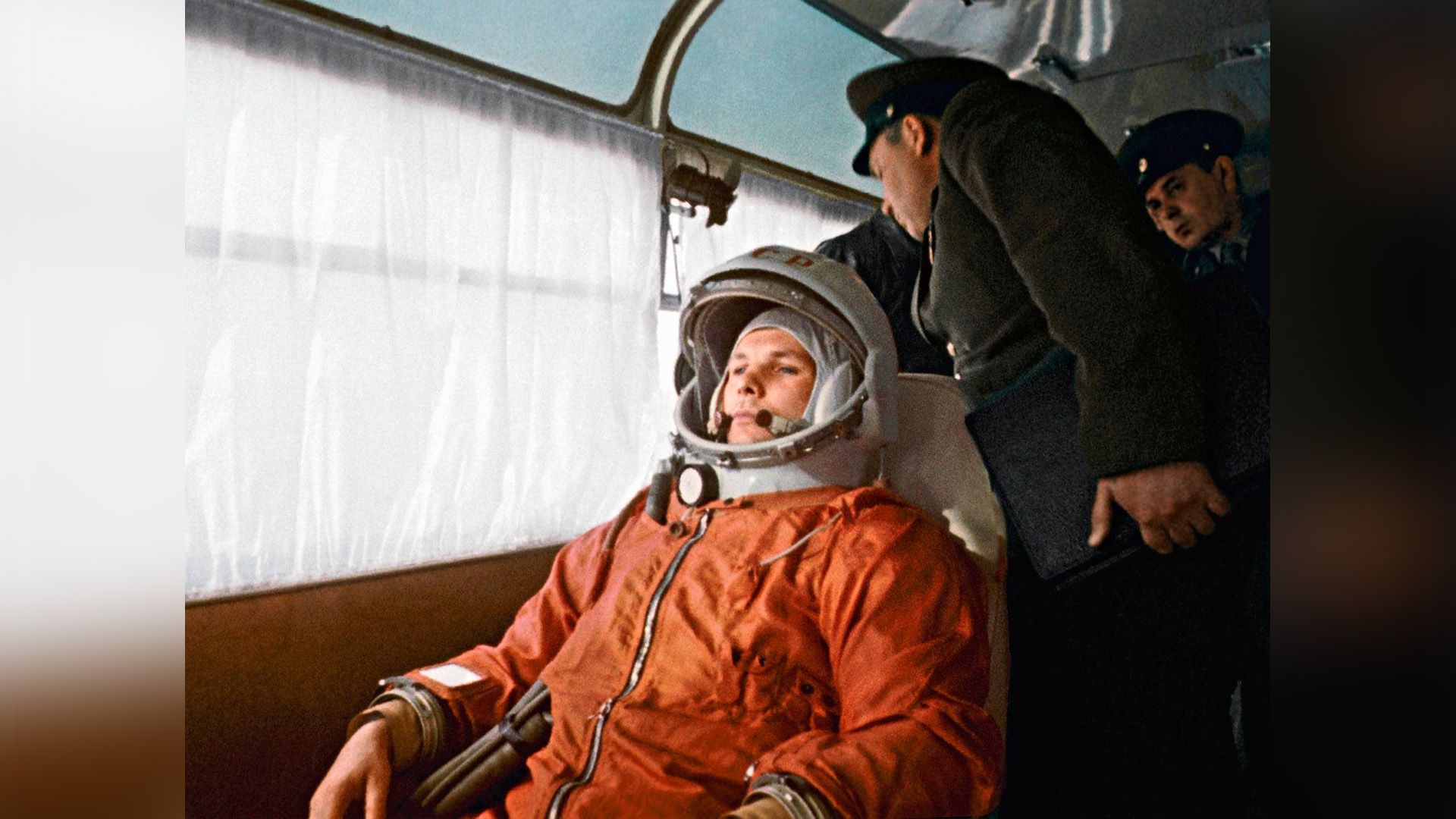Юрий Гагарин в оранжевом комбинезоне и белом скафандре сидит в кресле