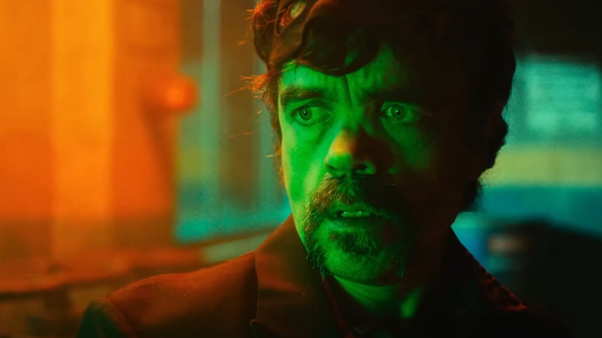 Питер Динклэйдж стоит в тёмном помещении, освещённый зелёным и оранжевым светом
