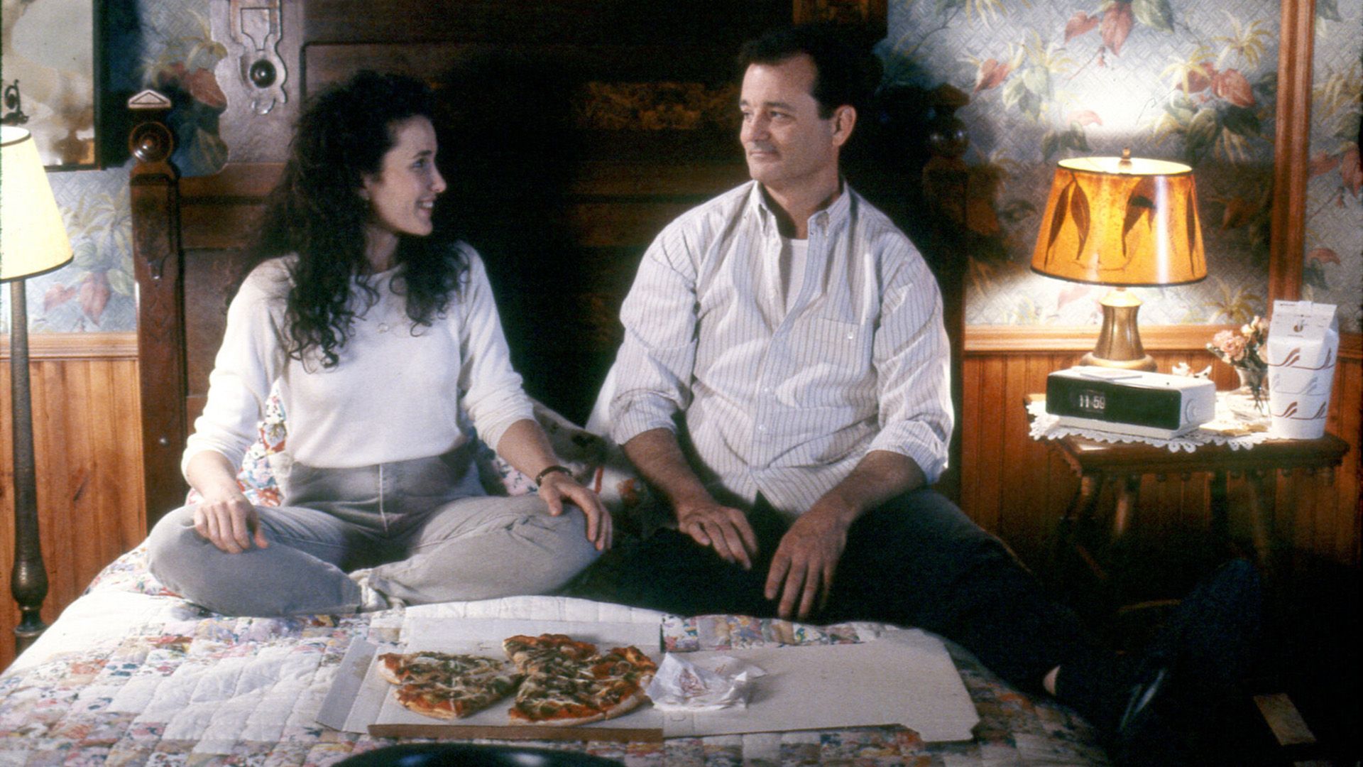 Энди МакДауэлл и Билл Мюррей сидят на кровати и смотрят друг на друга, перед ними открытая коробка с пиццей