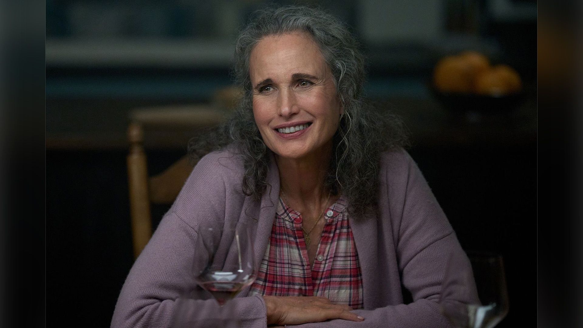 Энди МакДауэлл в сиреневой кофте сидит за обеденным столом и улыбается