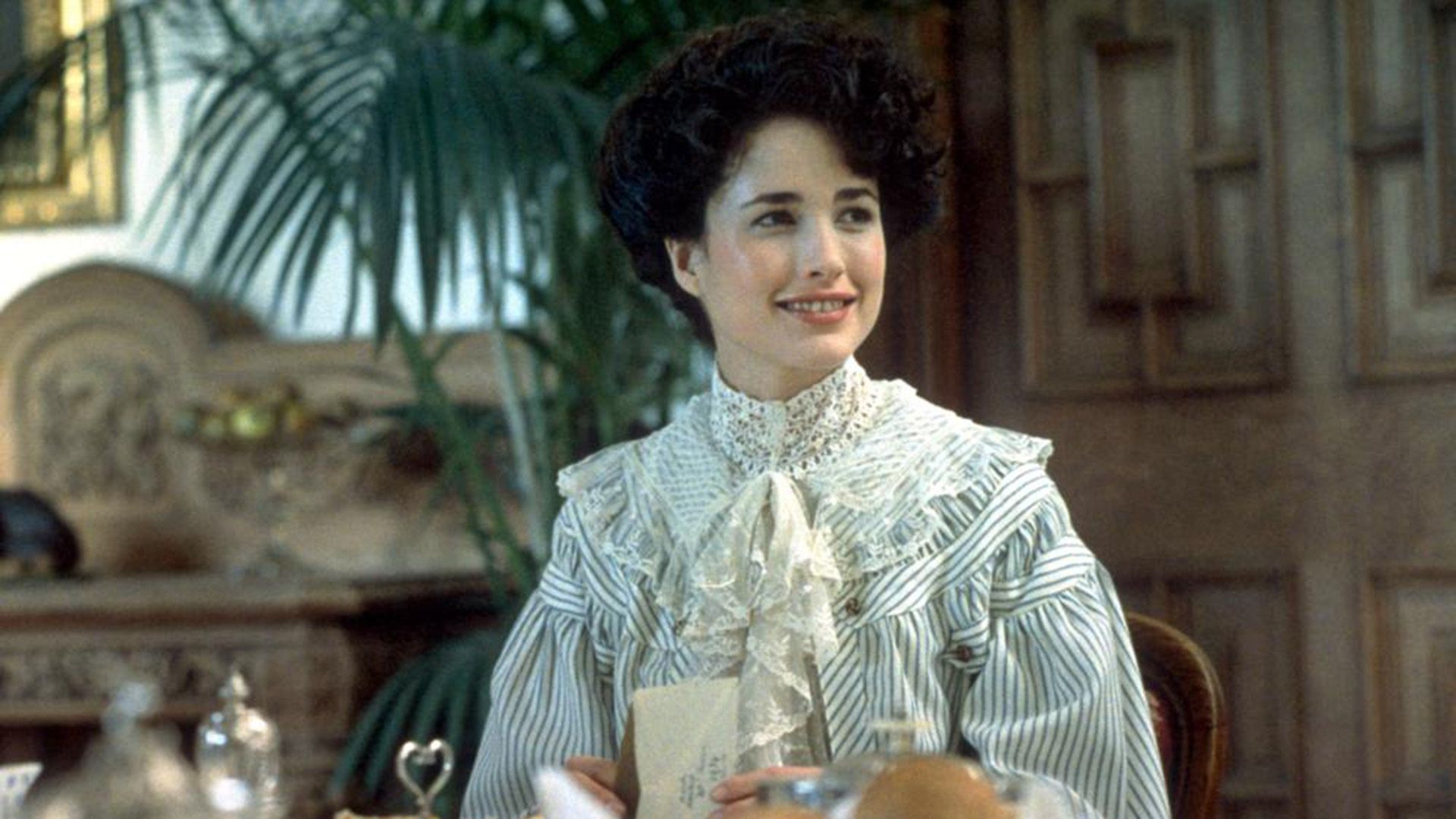 Энди МакДауэлл в полосатом платье с кружевным воротником сидит за обеденным столом