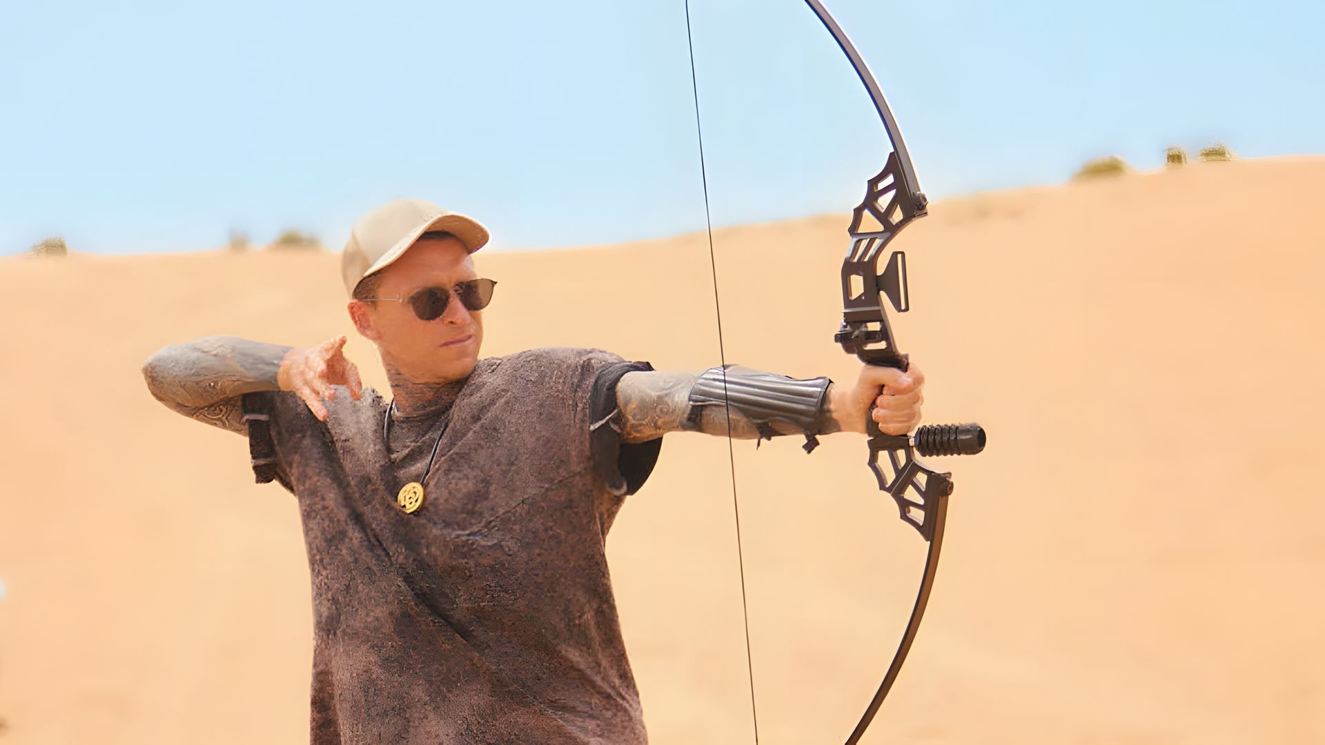 Павел Мамаев стреляет из лука на фоне барханов