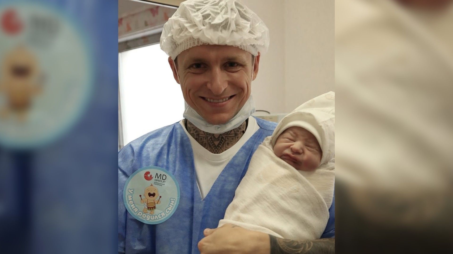 Павел Мамаев в медицинской шапочке держит на руках младенца