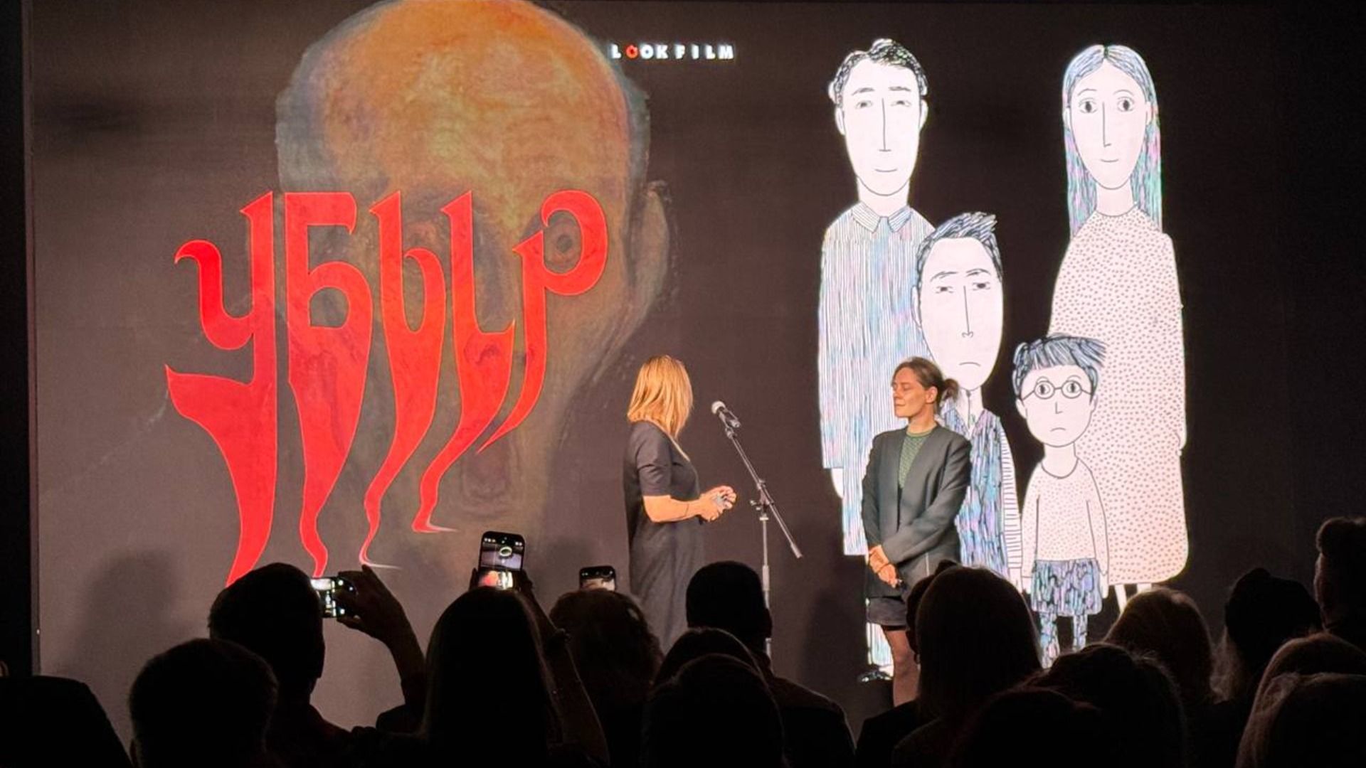 Фото из кинотеатра, на котором на сцене стоят люди, а на экране мултяшная семья