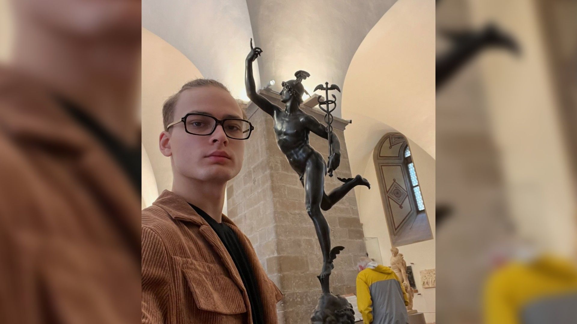 Ильдар Гайнутдинов в очках смотрит в камеру, на фоне античная скульптура