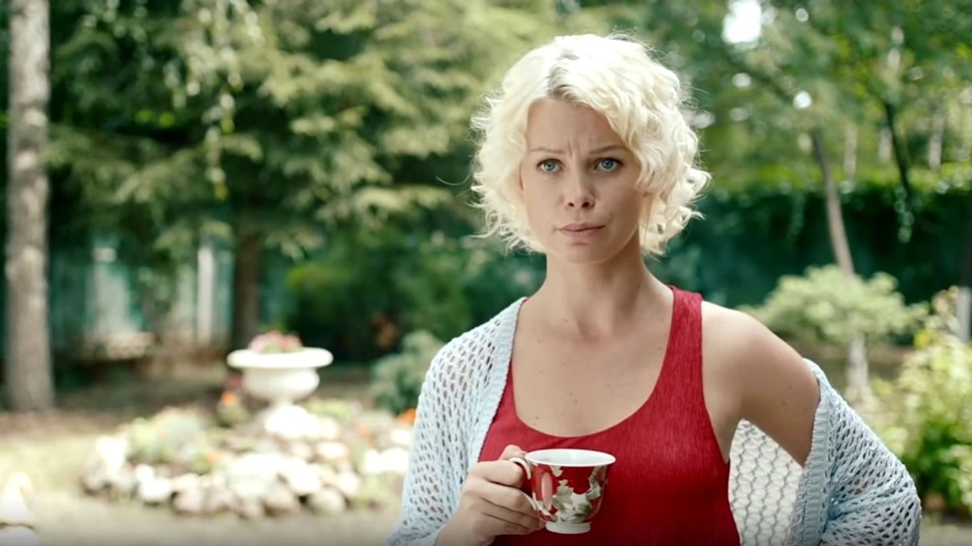 Евгения Осипова в красной майке и белом кардигане держит в руках кружку