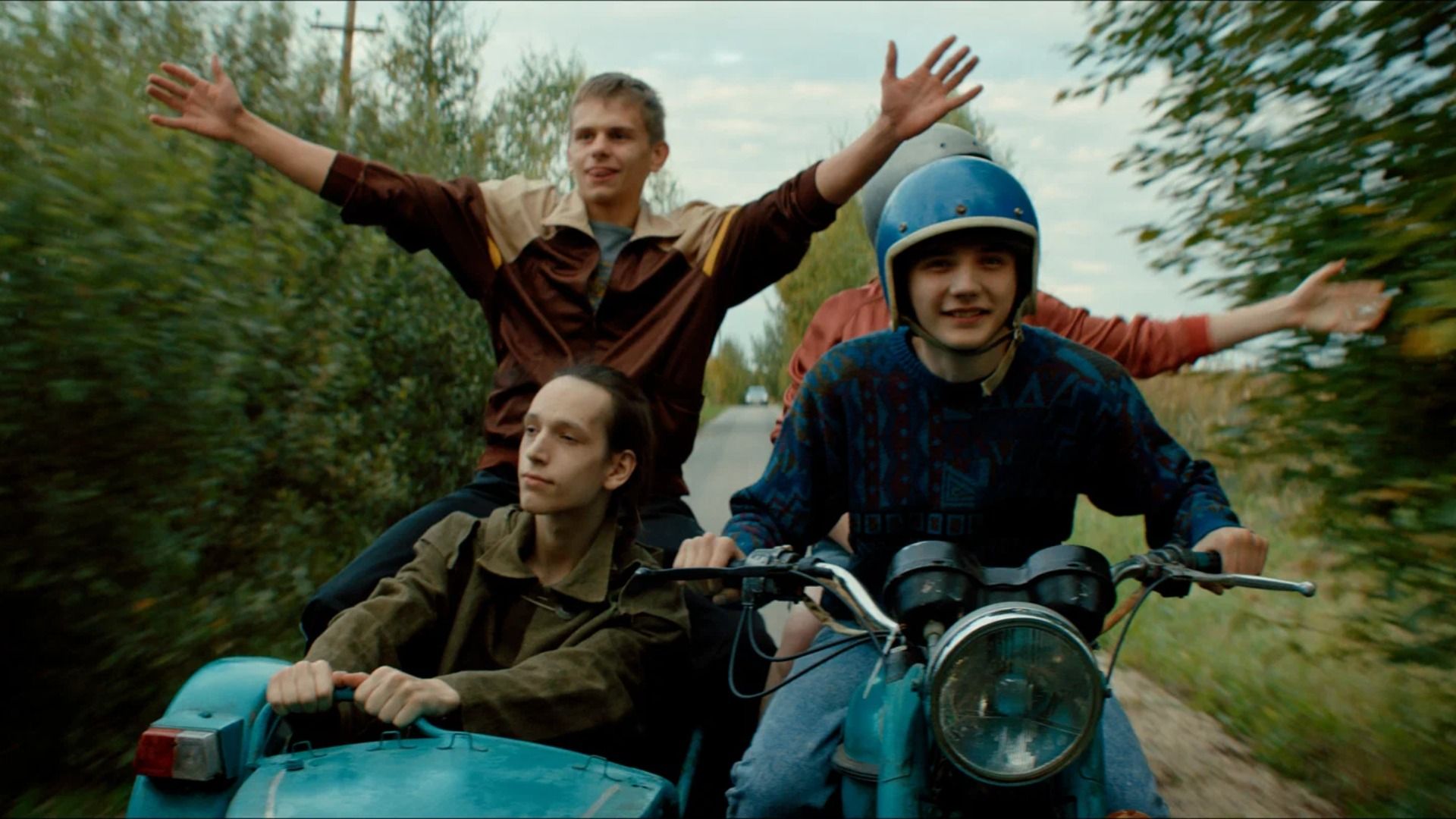 Группа подростков едет на мотоцикле среди деревьев