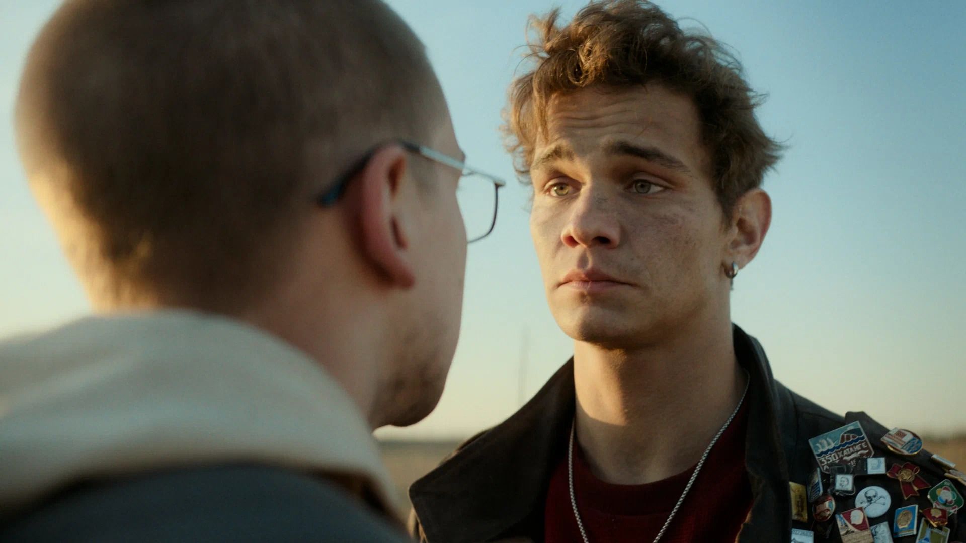 Лысый парень в очках стоит спиной, перед ним парень в кожаной куртке