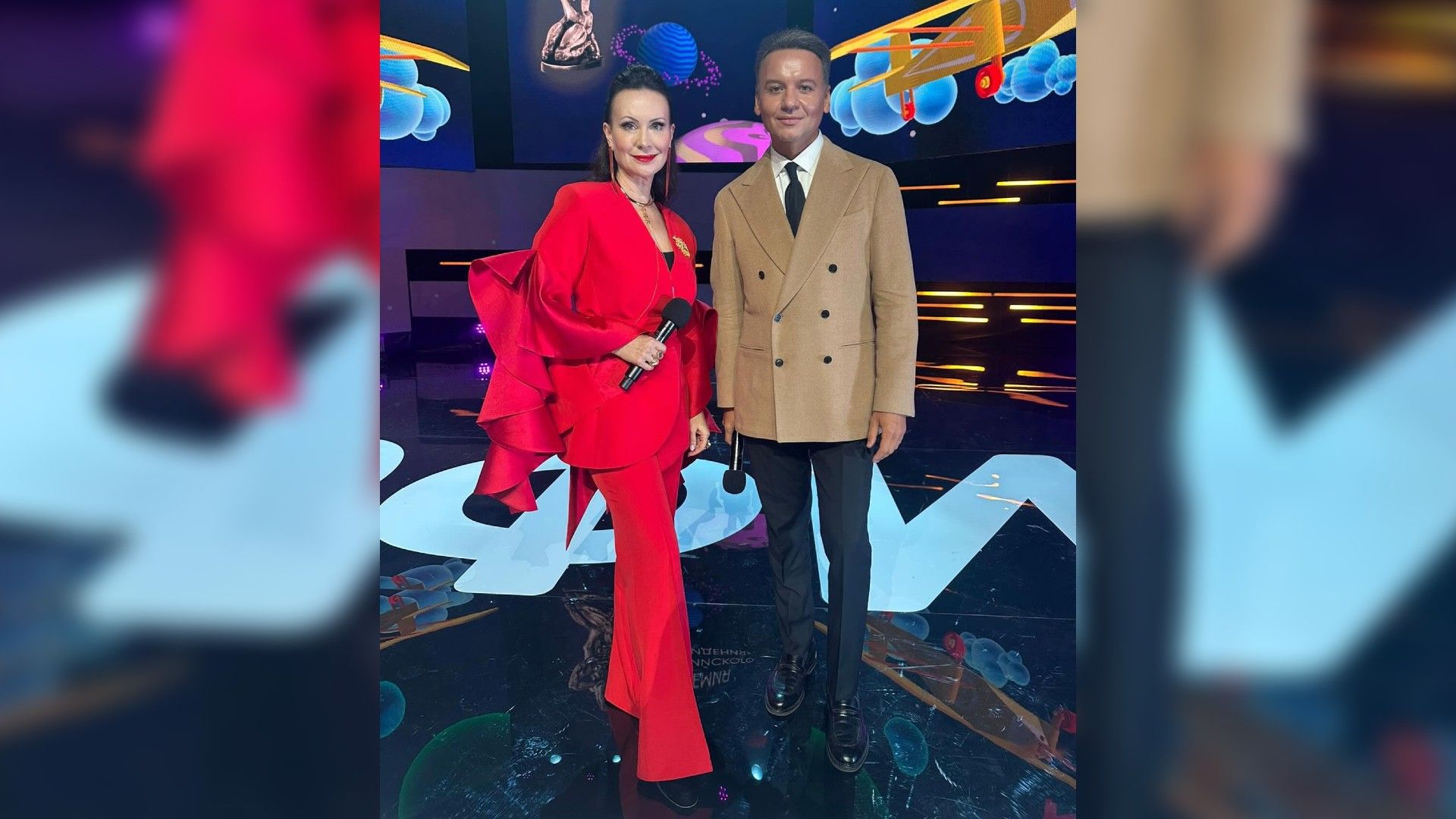 Александр Олешко и Нонна Гришаева позируют для камеры в полный рост на фоне надписи "Академия российского телевидения"