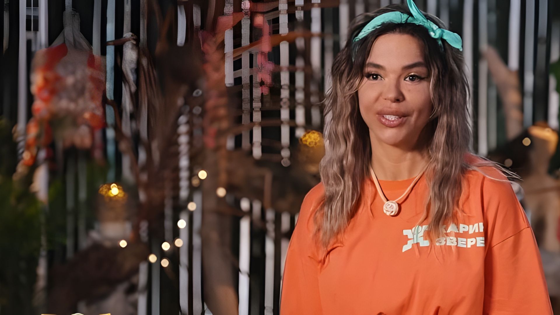 Карина Зверева в оранжевой футболке и головной повязке улыбается на камеру