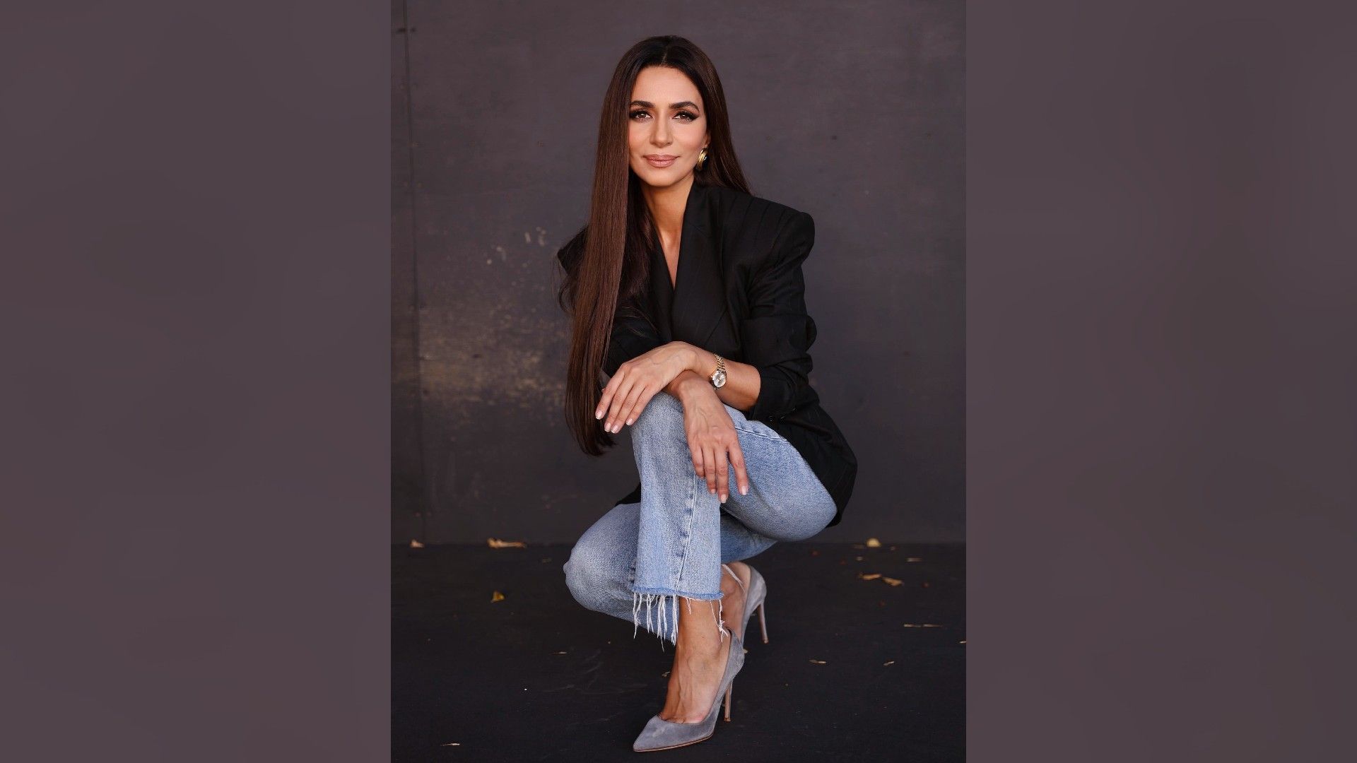 Певица Зара в джинсах сидит на корточках у стены