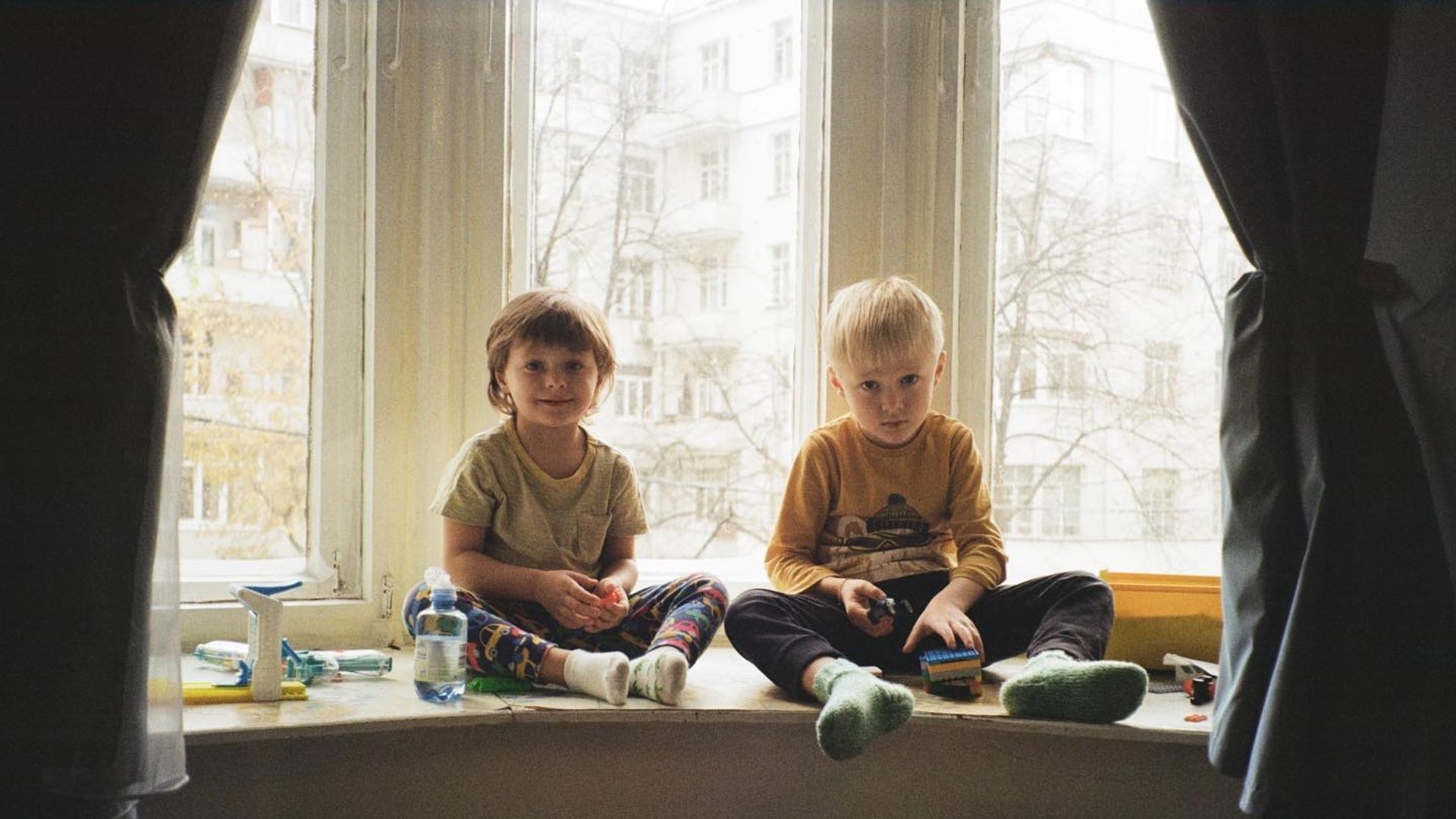 Два маленьких мальчика сидят на подоконнике и улыбаются