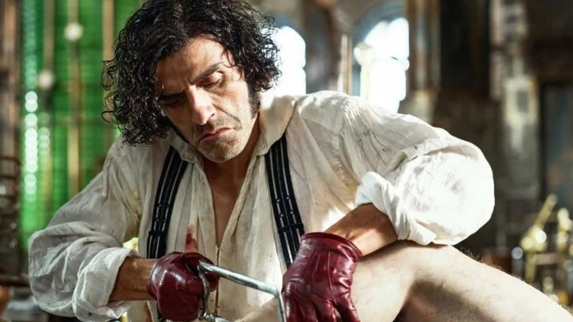 Оскар Айзек в одежде викторианской эпохи и красных кожаных перчатках держит в руках ножовку