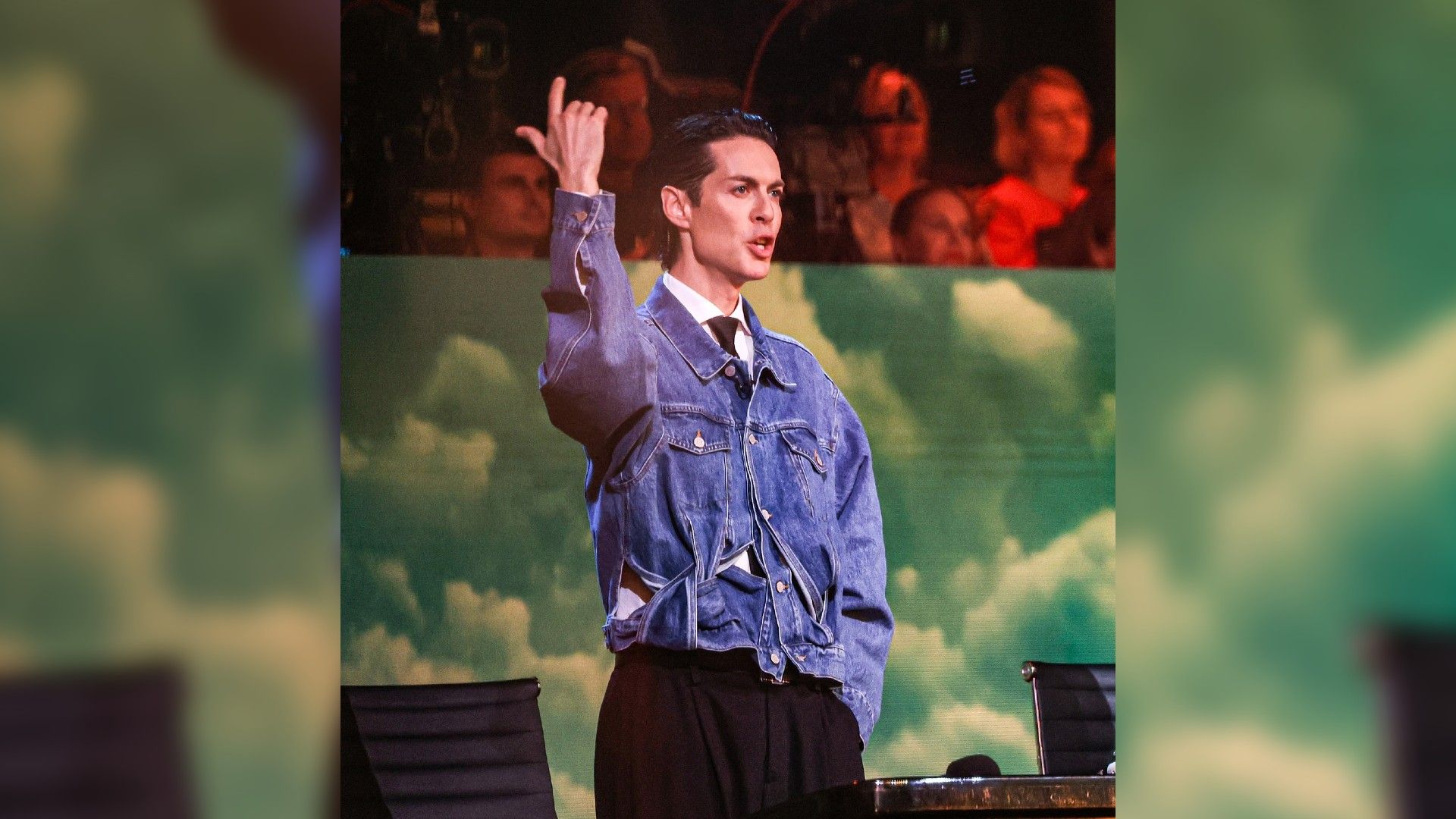 Марк Тишман в джинсовой куртке стоит, подняв палец вверх