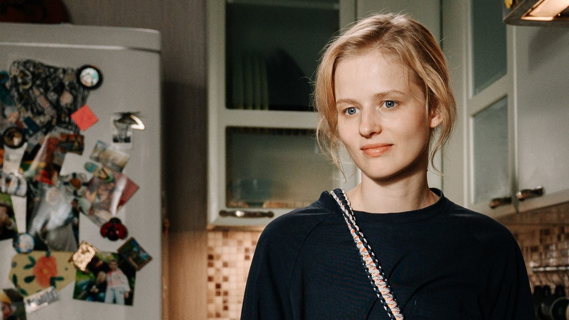 Александра Бортич в бордовой кофте стоит на кухне