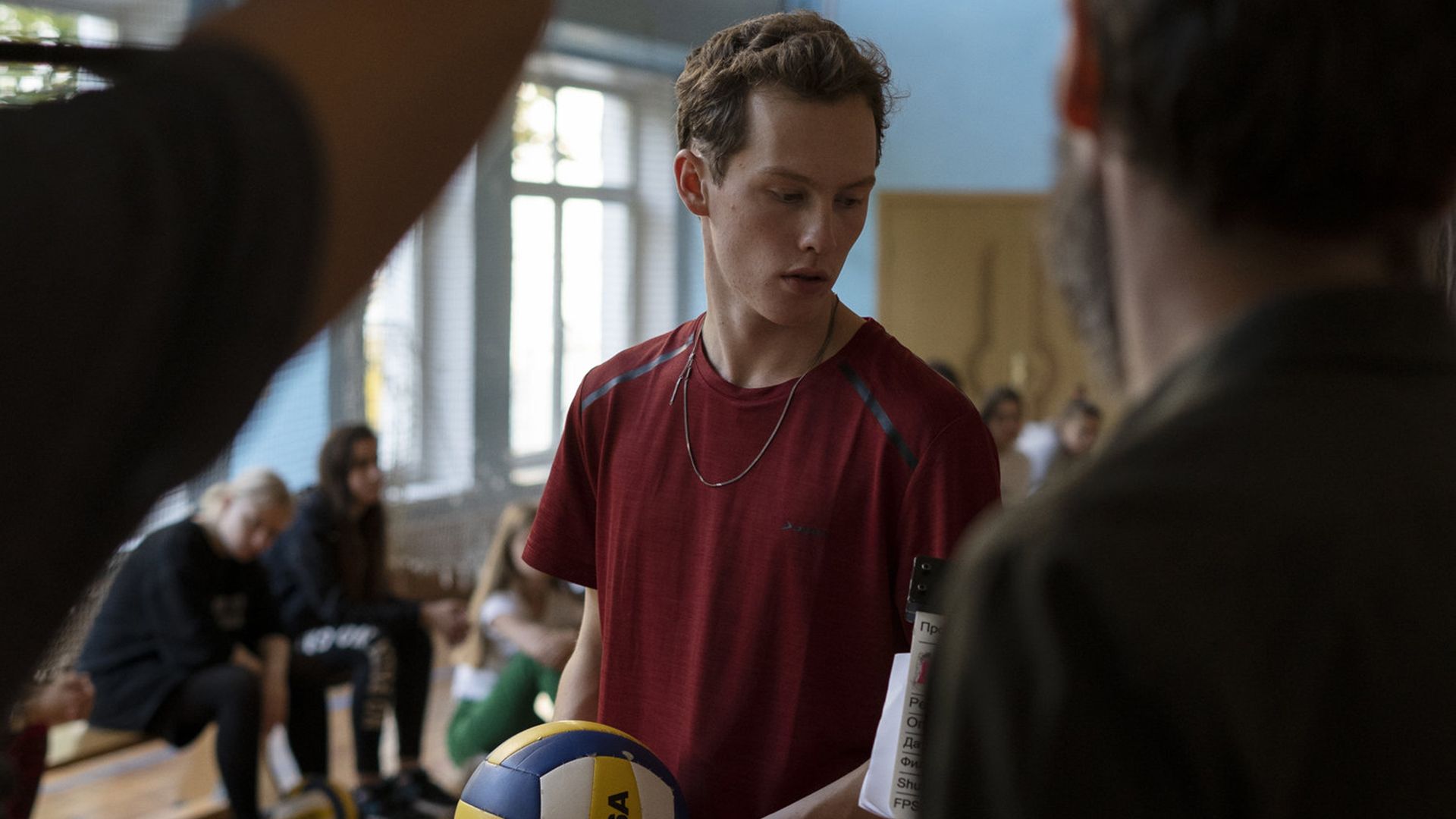 Илларион Маров в красной футболке и с мячом в руках стоит в школьном спортзале