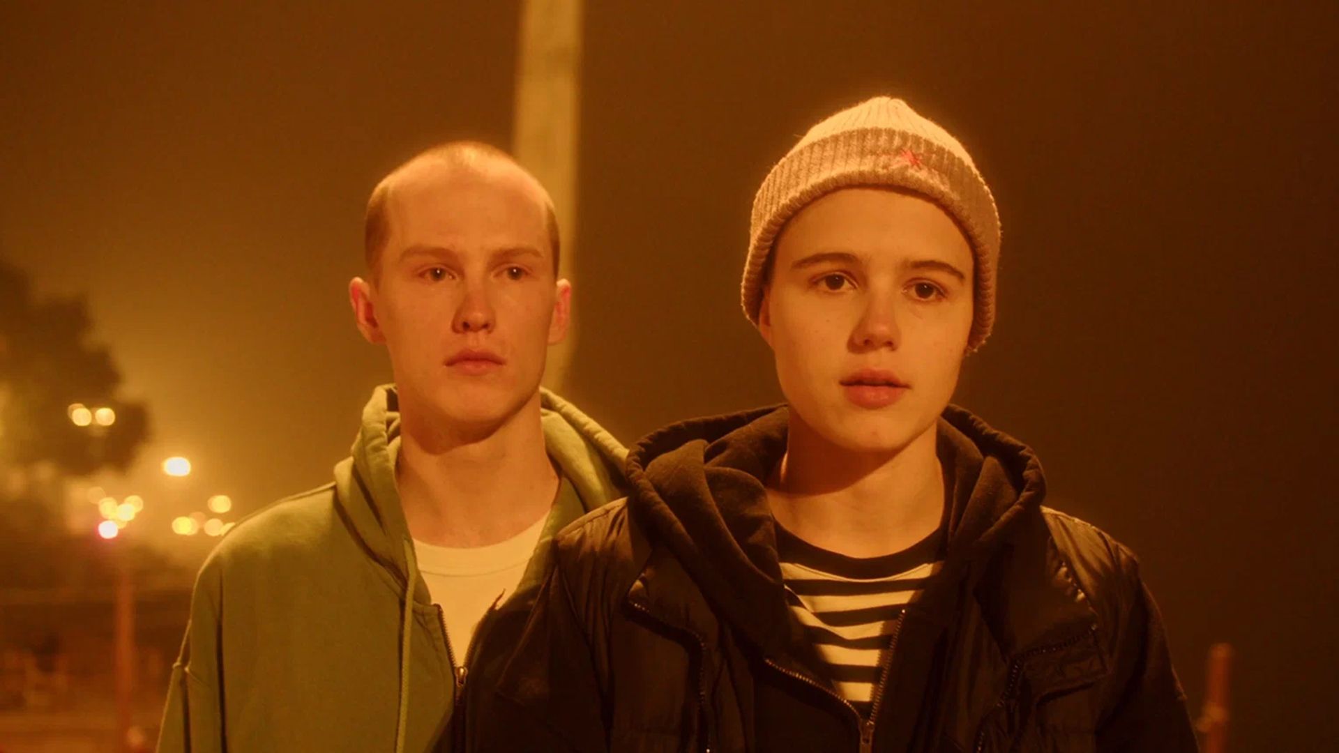 Илларион Маров стоит рядом с Марией Мацель, одетой в куртку и шапку, всё залито оранжевым светом