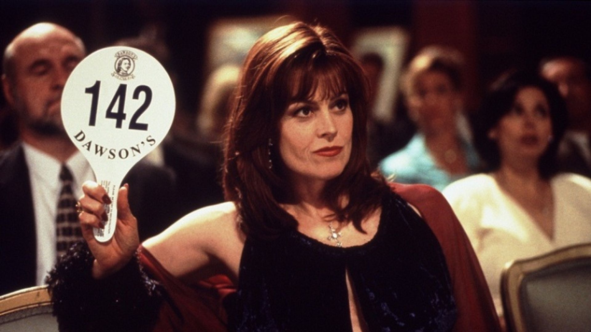 Сигурни Уивер в вечернем платье поднимает табличку аукциона