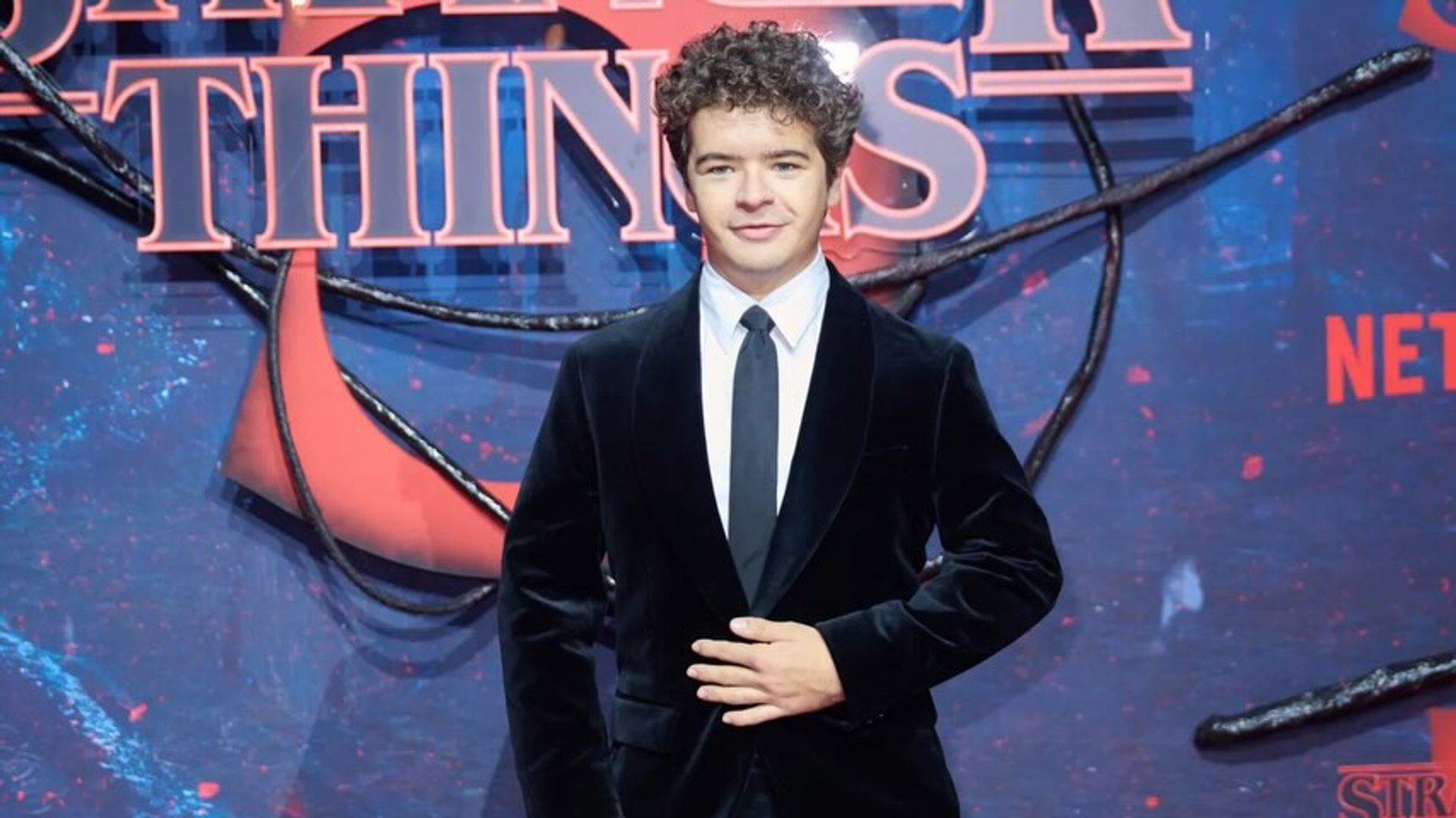 Гейтен Матараццо в костюме на фоне надписи "Очень странные дела"