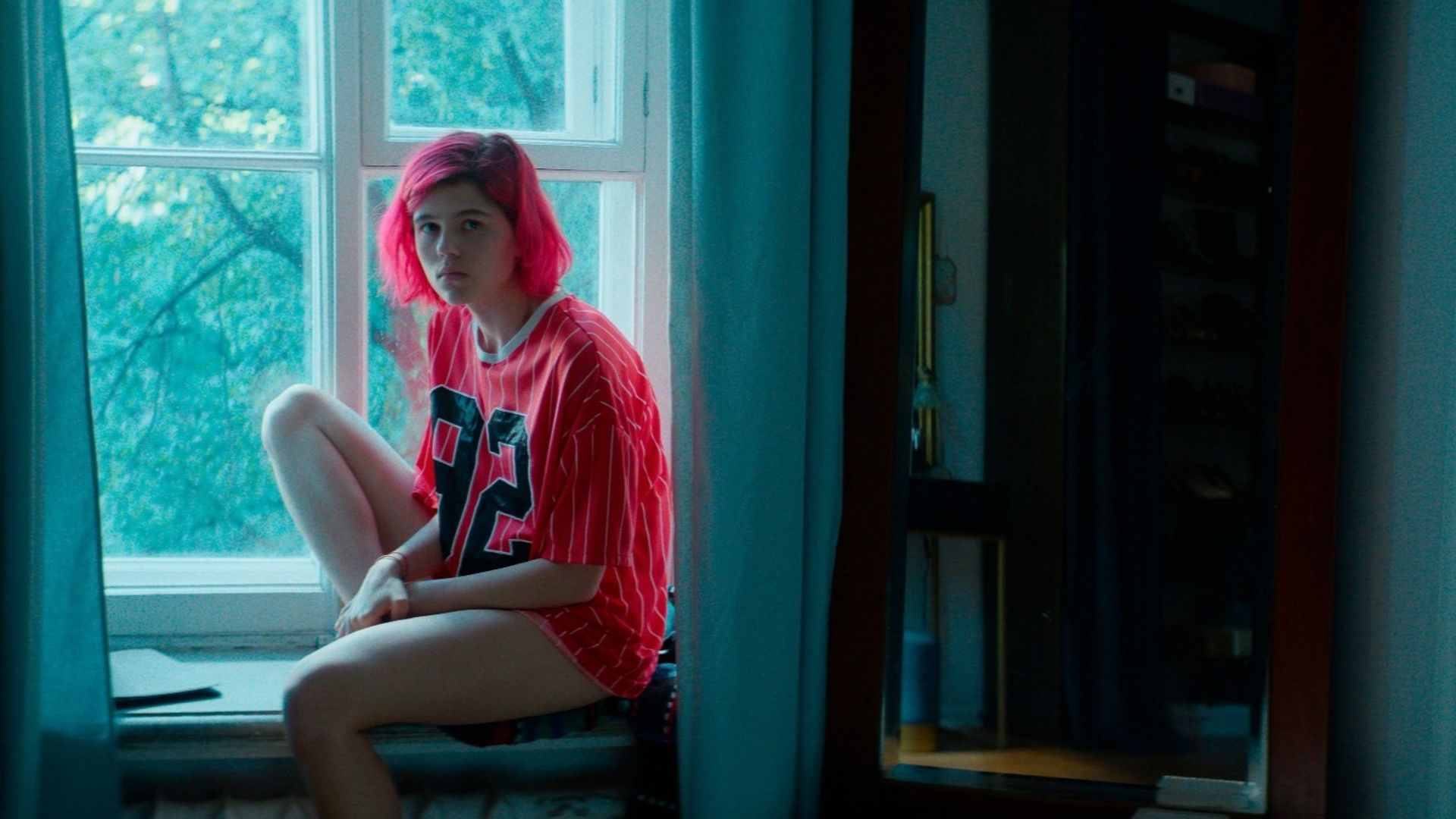 Мария Мацель с розовыми волосами сидит на подоконнике