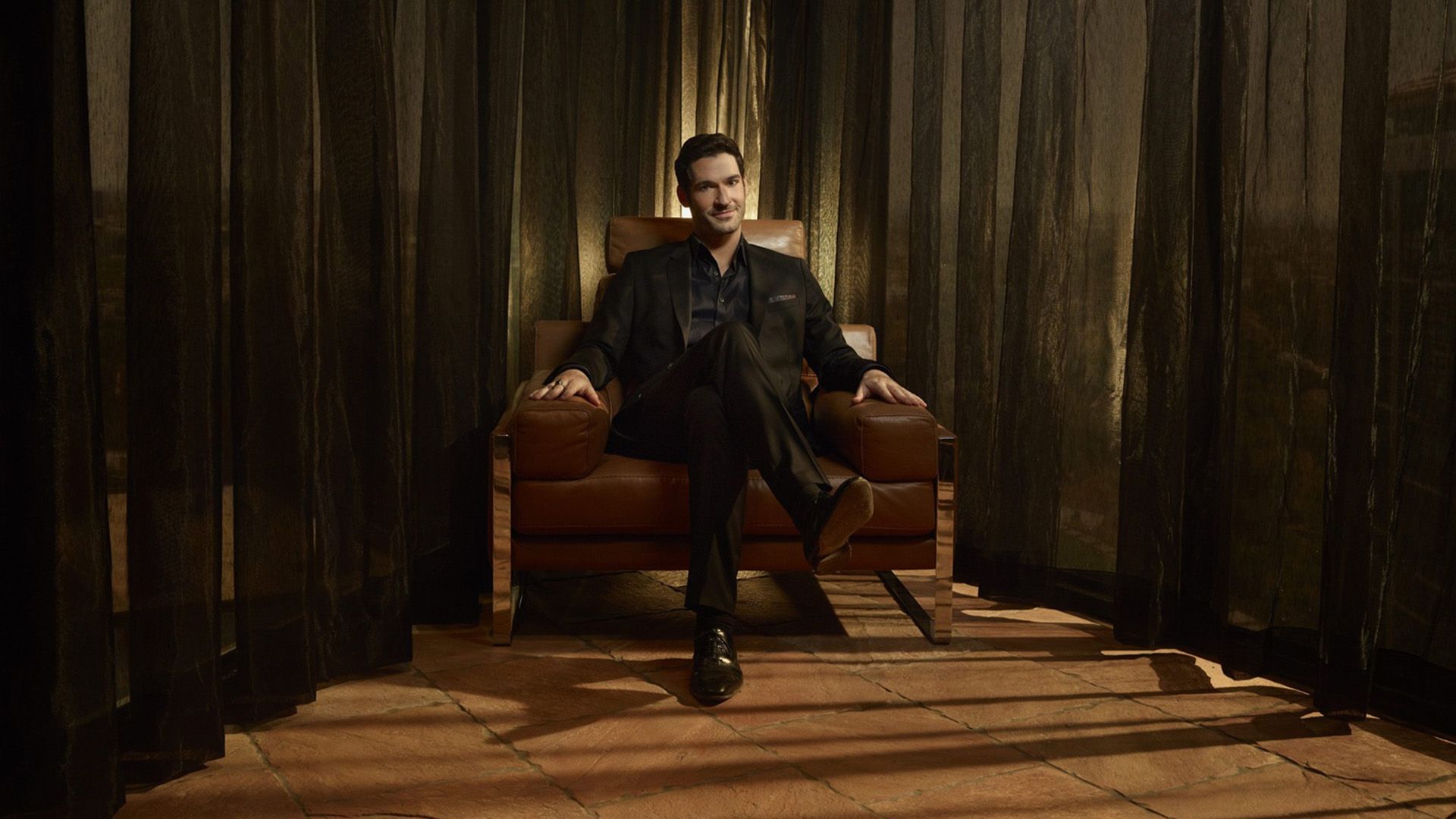 Том Эллис сидит в кожаном кресле, закинув ногу на ногу