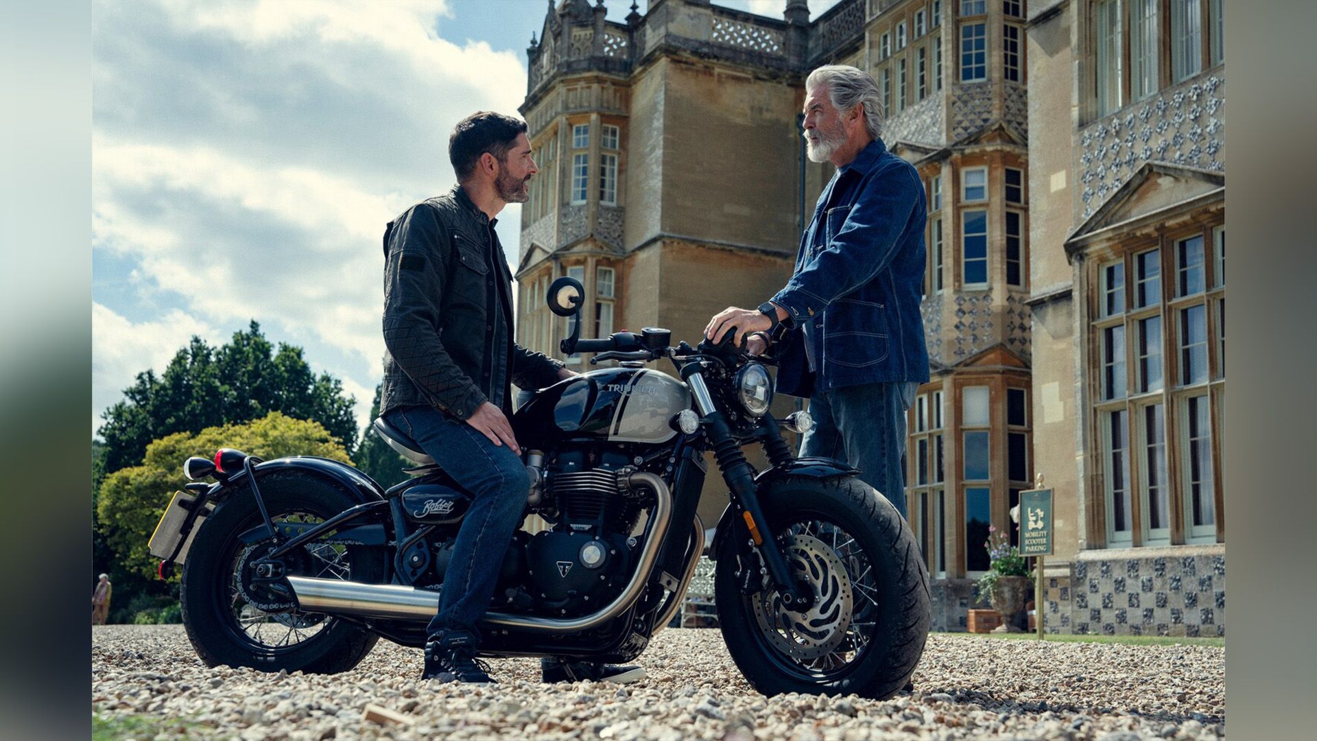 Том Эллис, сидя на мотоцикле, разговаривает с Пирсом Броснаном, стоящим рядом