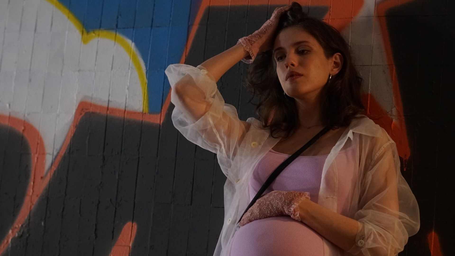 Анна Чиповская стоит, оперевшись о стену, с накладным животом