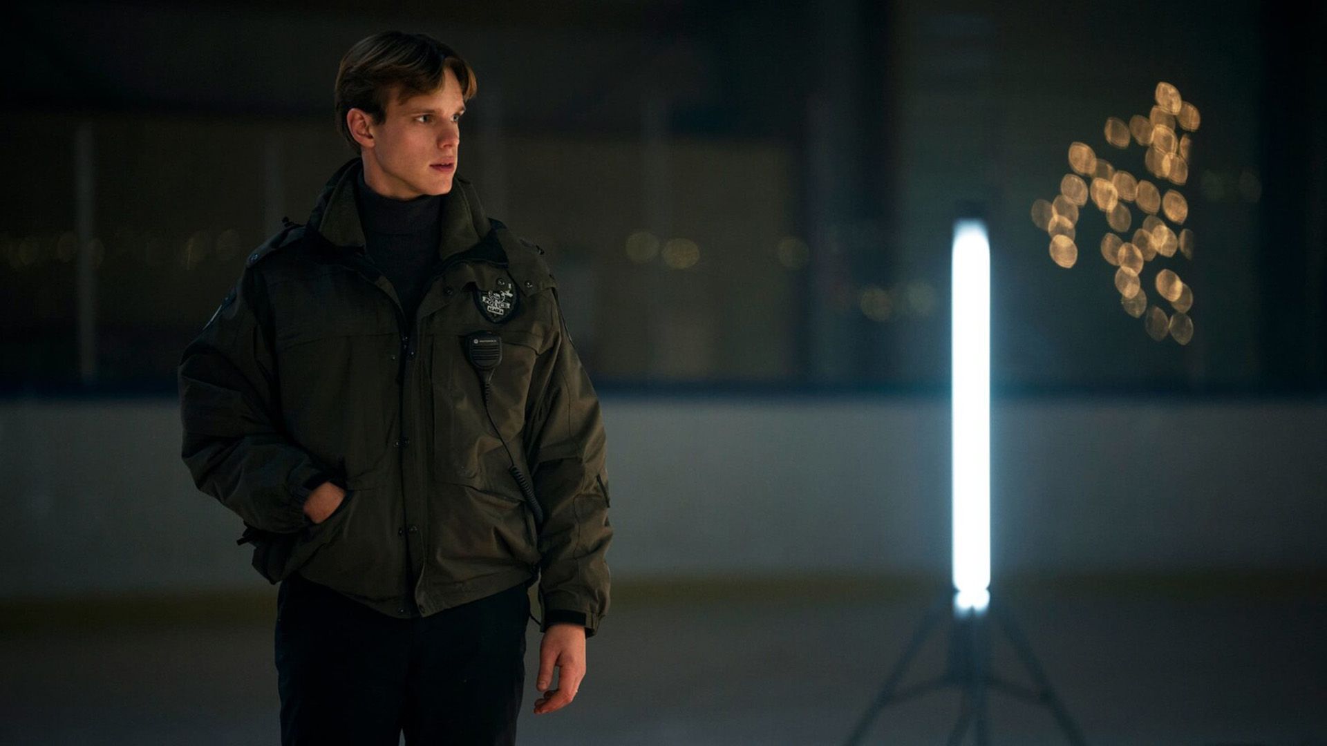 Финн Беннетт в полицейской униформе стоит рядом с большой лампой дневного света