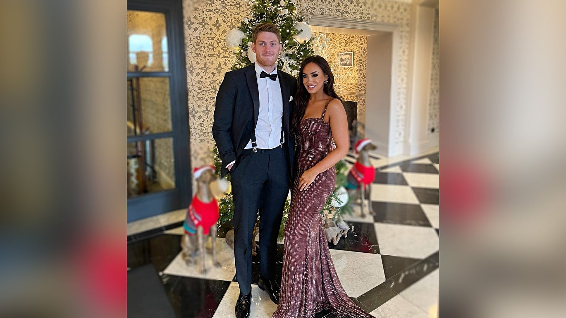 Питер Клэффи в смокинге и его девушка Элли в блестящем вечернем платье позируют на фоне рождественской ели